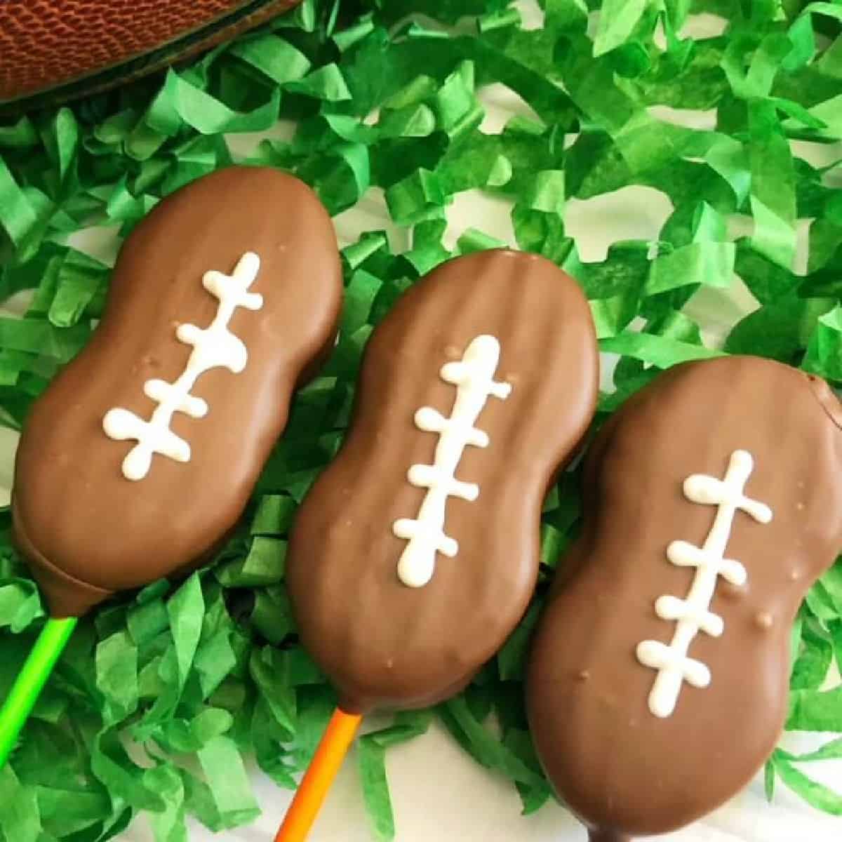 Close up image of football cookie pops on green confetti. 