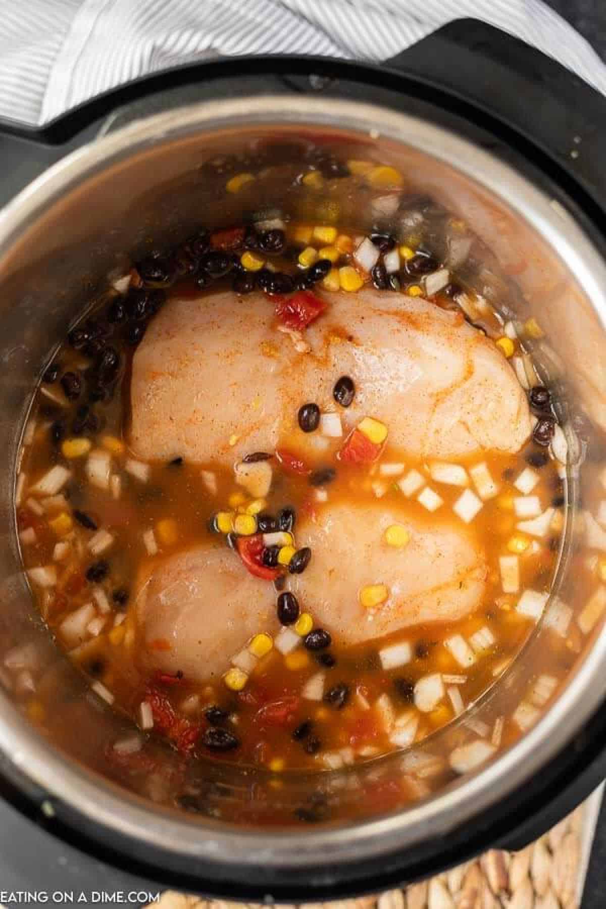 Chicken in the instant pot topped with black beans, corn and diced onions in a broth