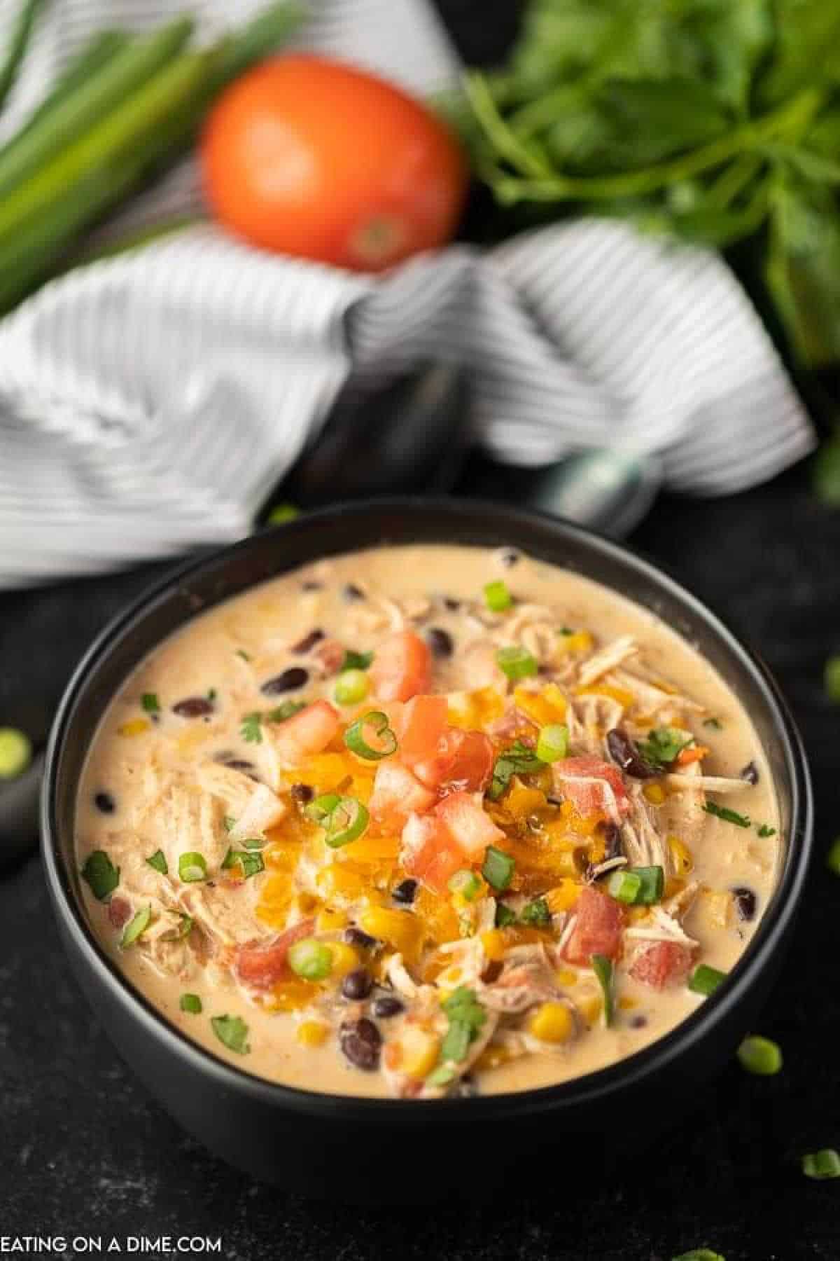 Chicken tortilla soup in a black bowl topped with shredded cheese, diced tomatoes and chopped green onions