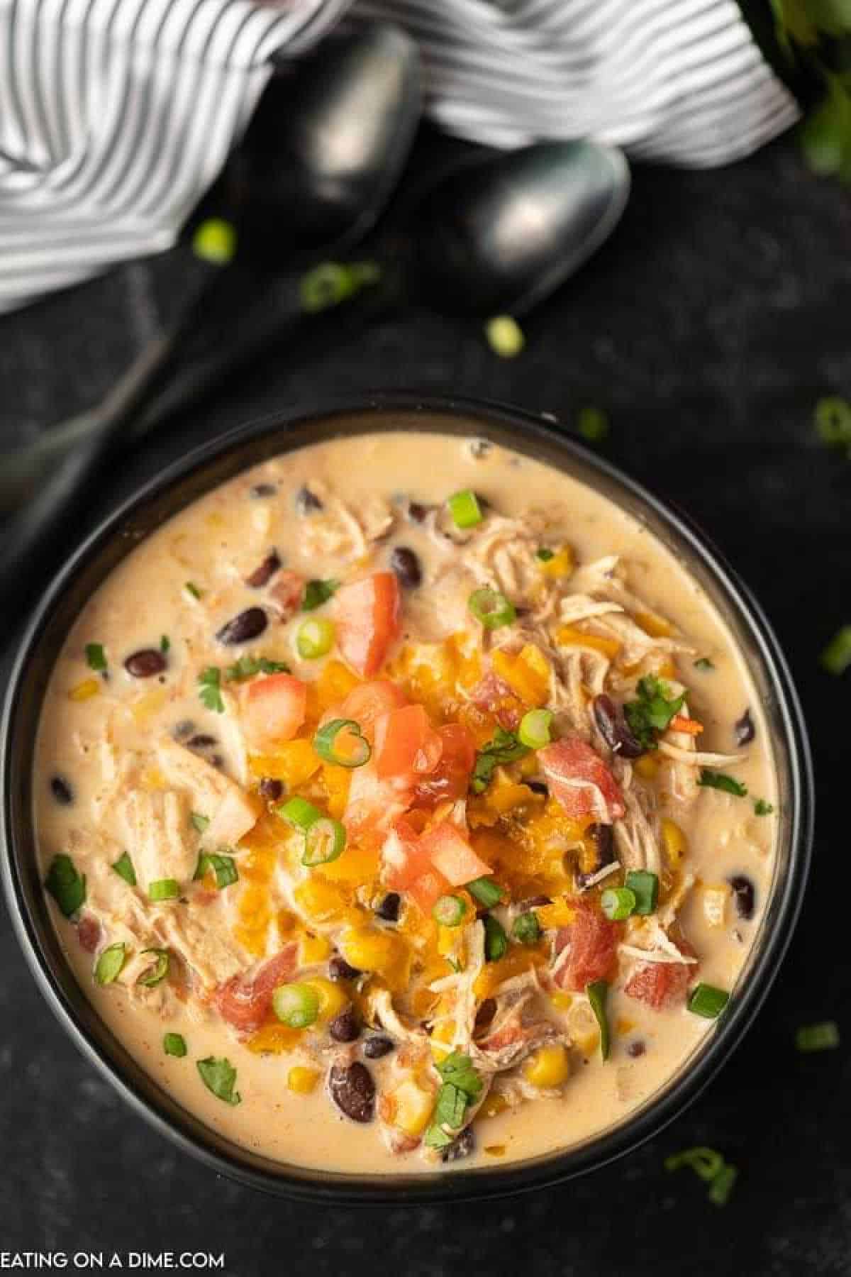 Creamy chicken tortilla soup in a bowl topped with shredded cheese, green onions and diced tomatoes