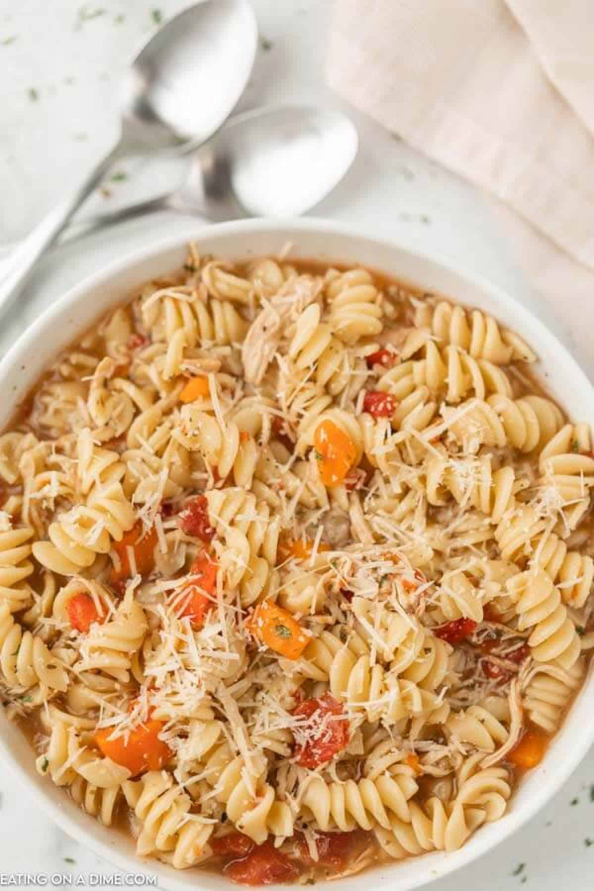 Close up image of a bowl of Italian Chicken Soup in a white bowl with two spoons. 