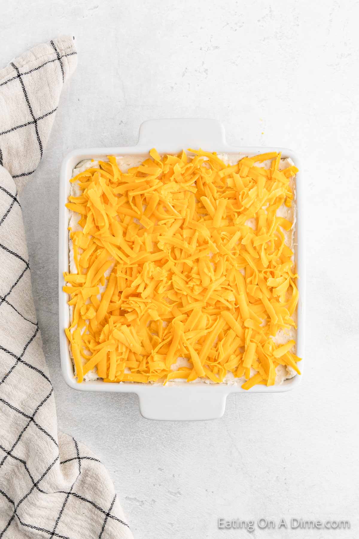 Topping mashed potatoes in casserole dish with shredded cheese