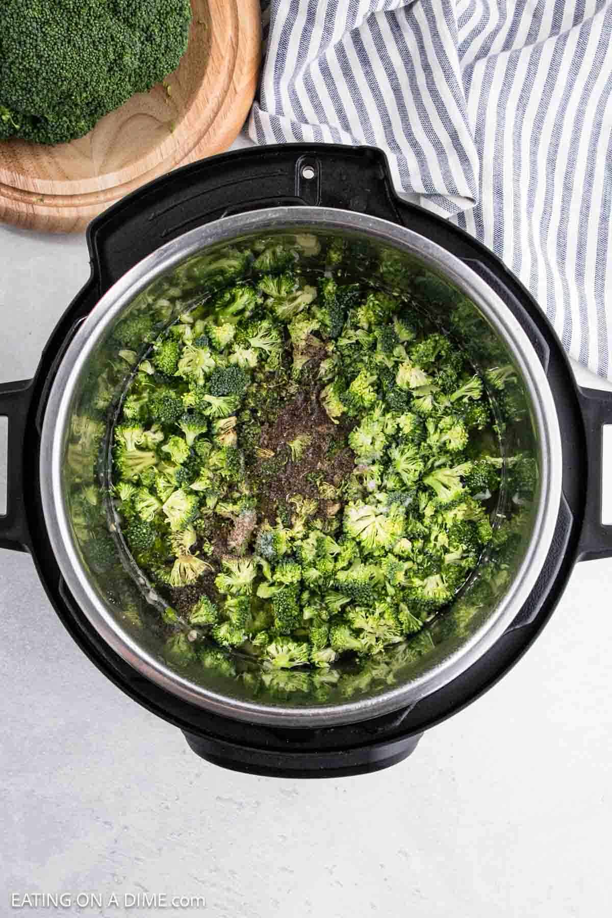 An overhead view of an Instant Pot shows chopped broccoli ready to be transformed into a delightful Broccoli Cheddar Soup. Nearby, a wooden cutting board with extra florets and a striped cloth await their turn to join the savory symphony.