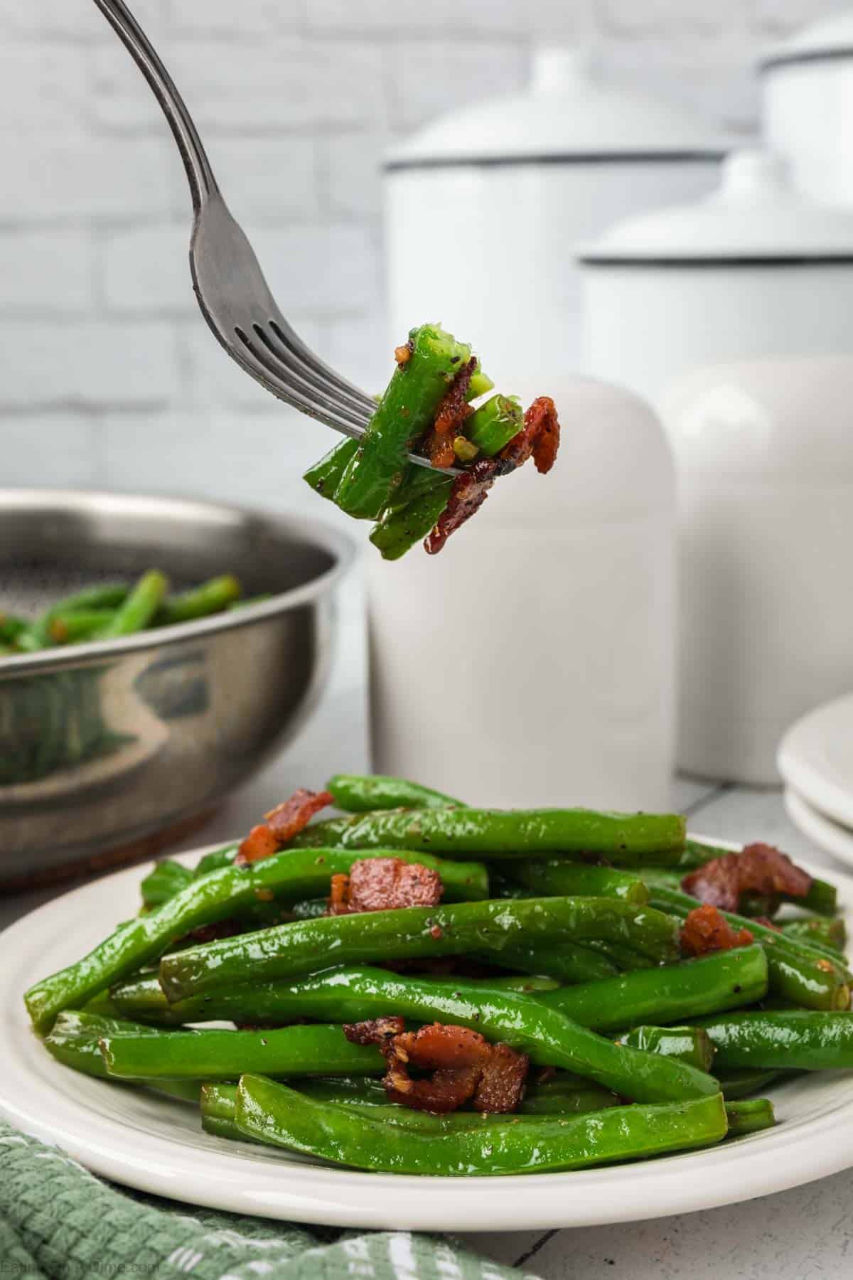 Cooked green beans on a plate with chopped cooked bacon with a serving on a fork