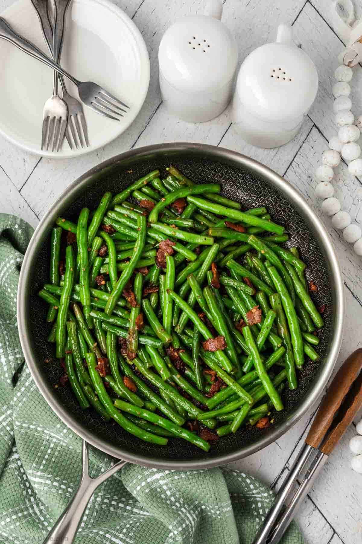 Cooked green beans with chopped bacon in a skillet