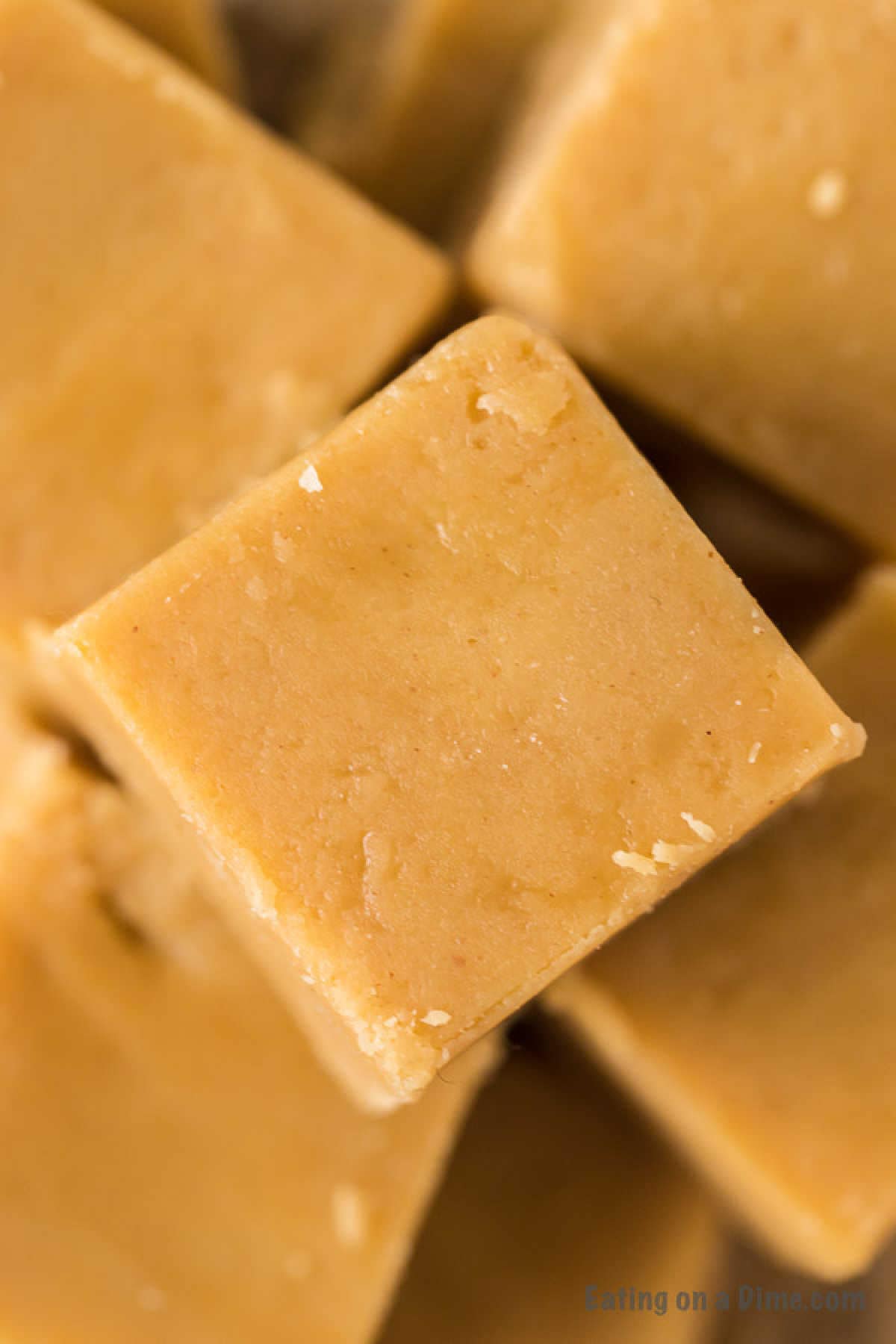 Close-up image of stacked pieces of creamy 3 Ingredient Peanut Butter Fudge. The fudge is light brown in color with a smooth texture and very slight crumbly edges.