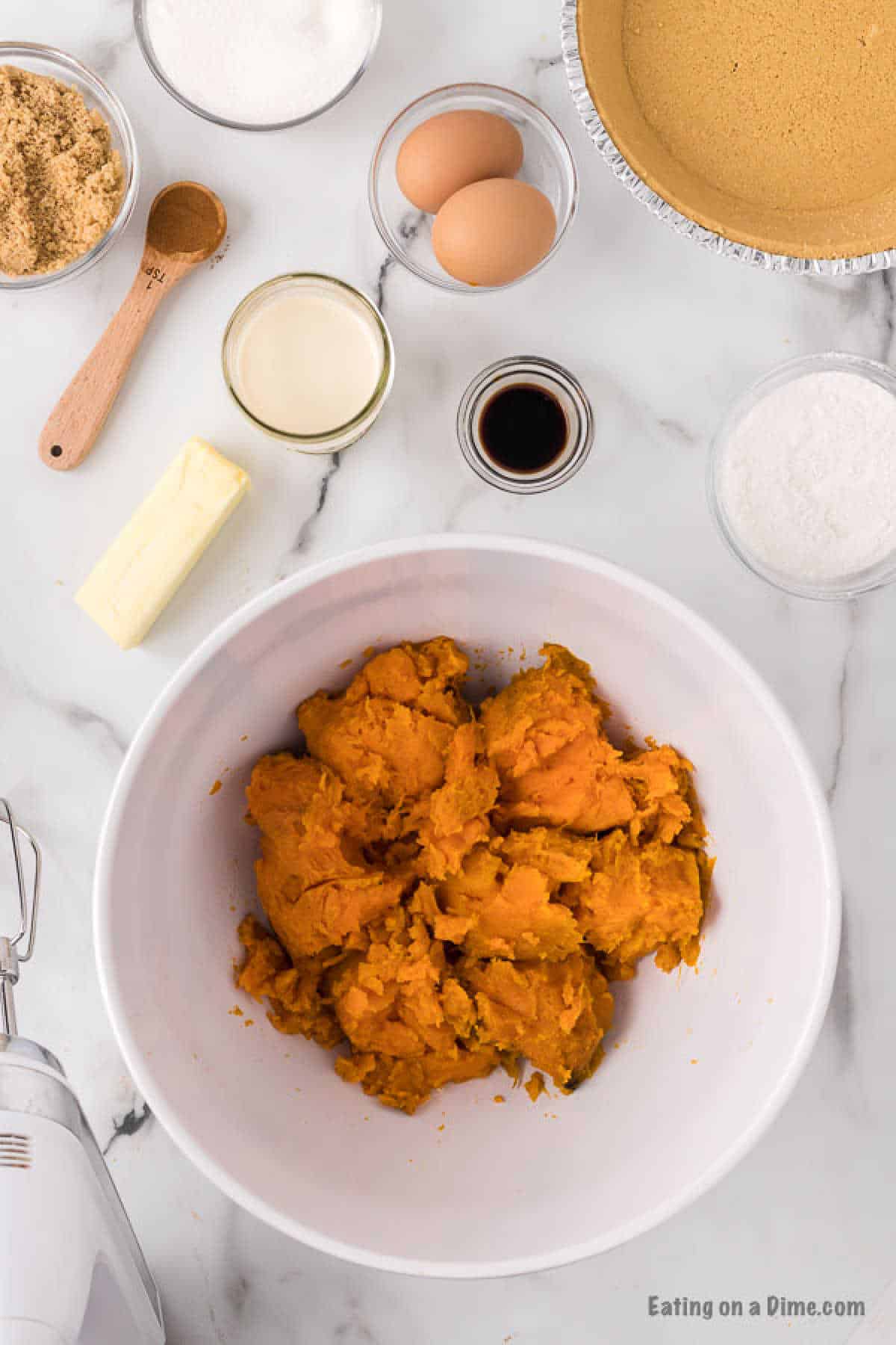 Mashed sweet potatoes in a bowl, stick of butter, eggs, brown sugar, cinnamon, vanilla, graham cracker