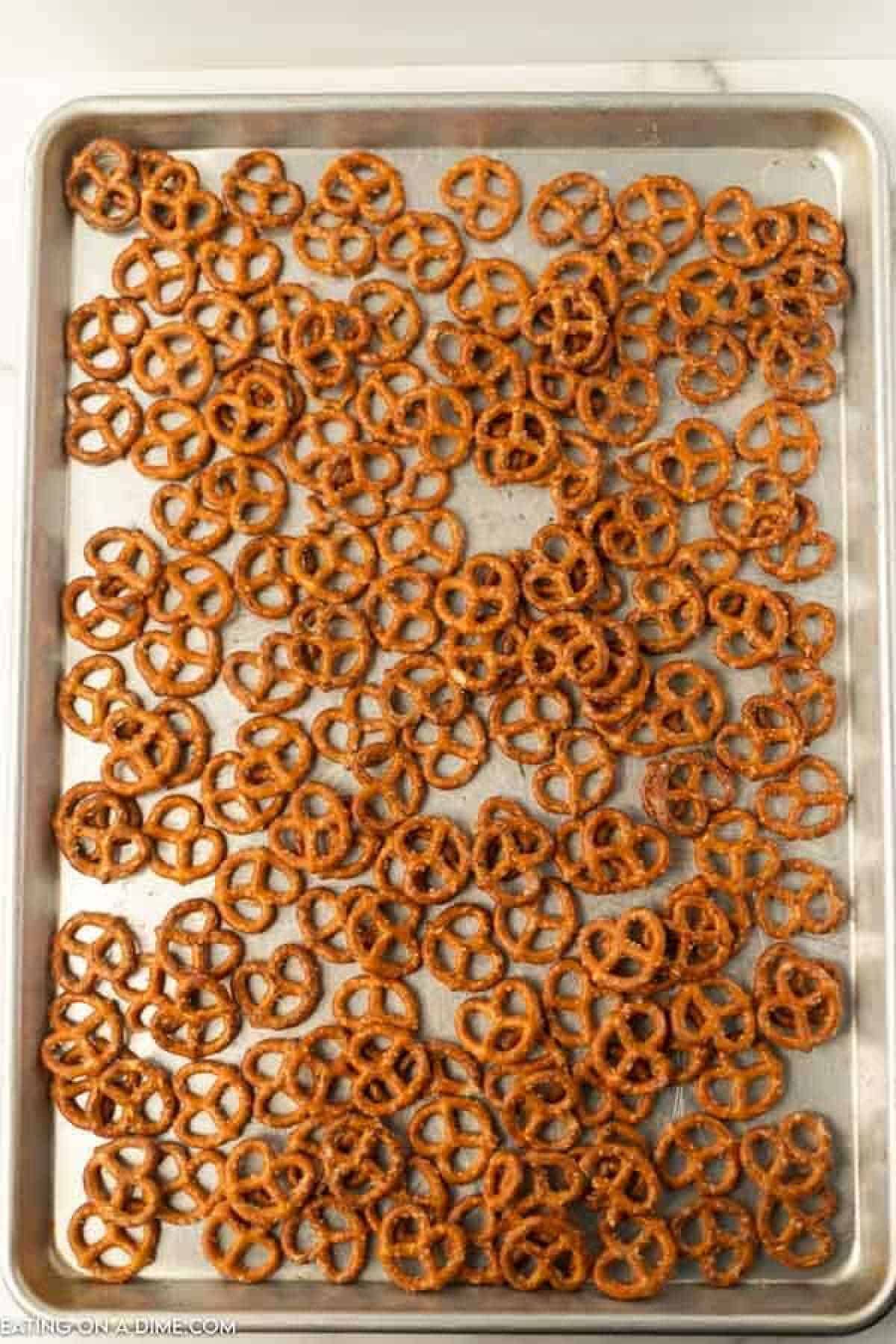 A baking sheet filled with small garlic ranch pretzels is spread out evenly across the tray. The pretzels have a shiny, lightly browned appearance. The background shows a marble surface, hinting at the delicious recipe behind these flavorful bites.