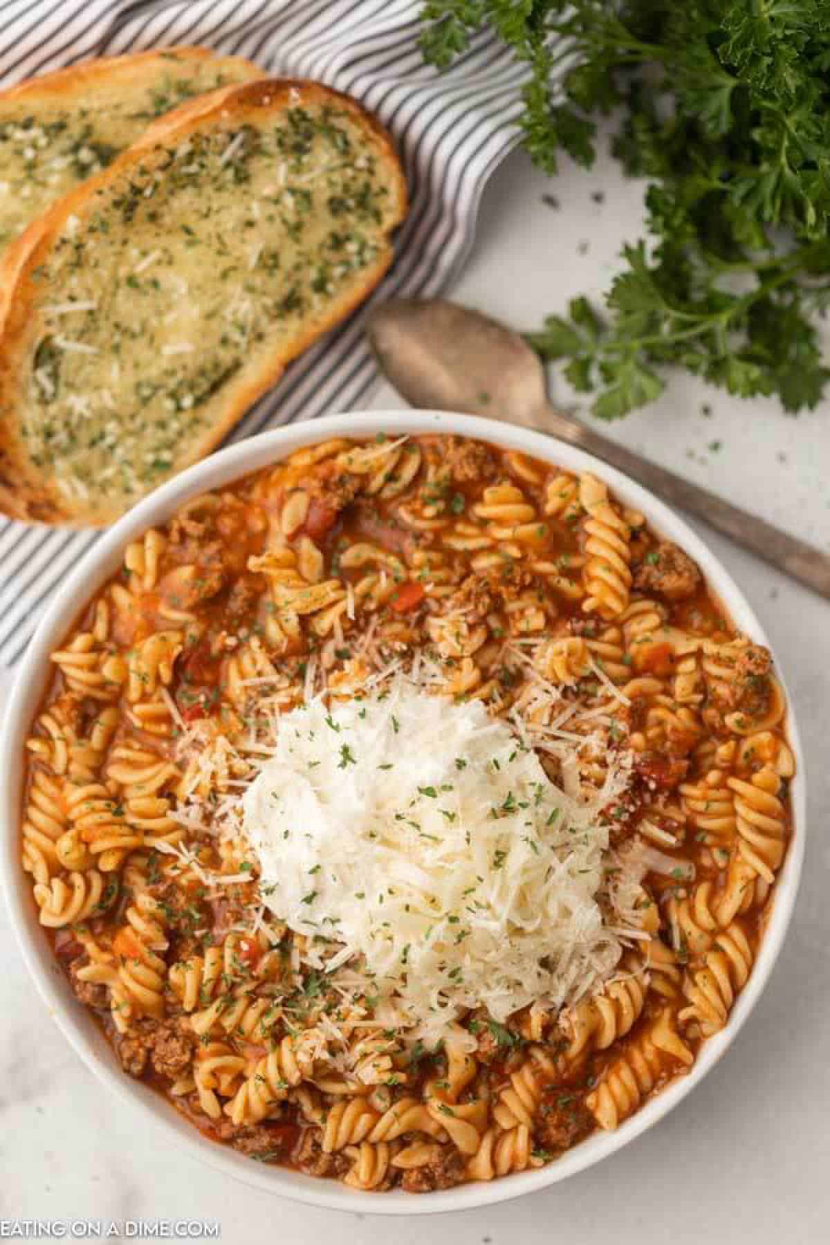 bowl of lasagna soup with a slice of french bread and spoon. Topped with shredded cheese, ricotta cheese