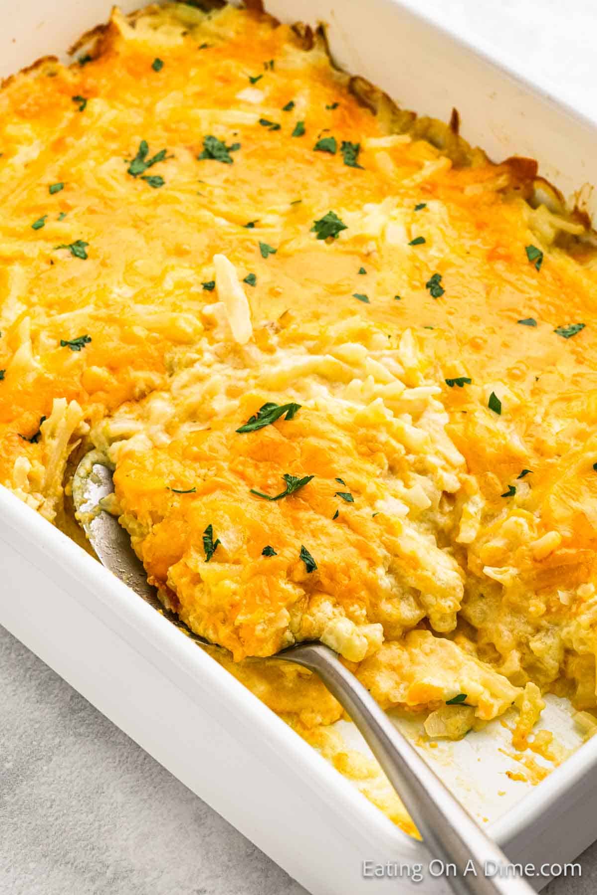 Cheesy potato casserole in a baking dish with a serving spoon