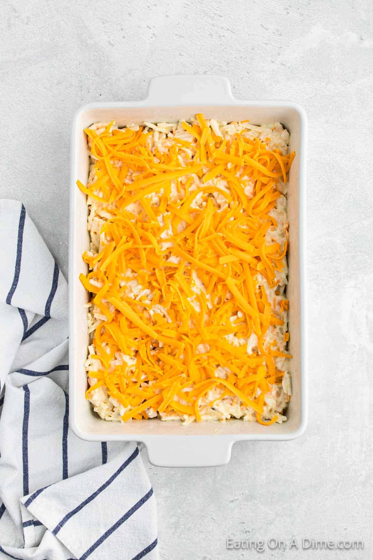 Shredded cheese topped with the potato casserole in the baking dish