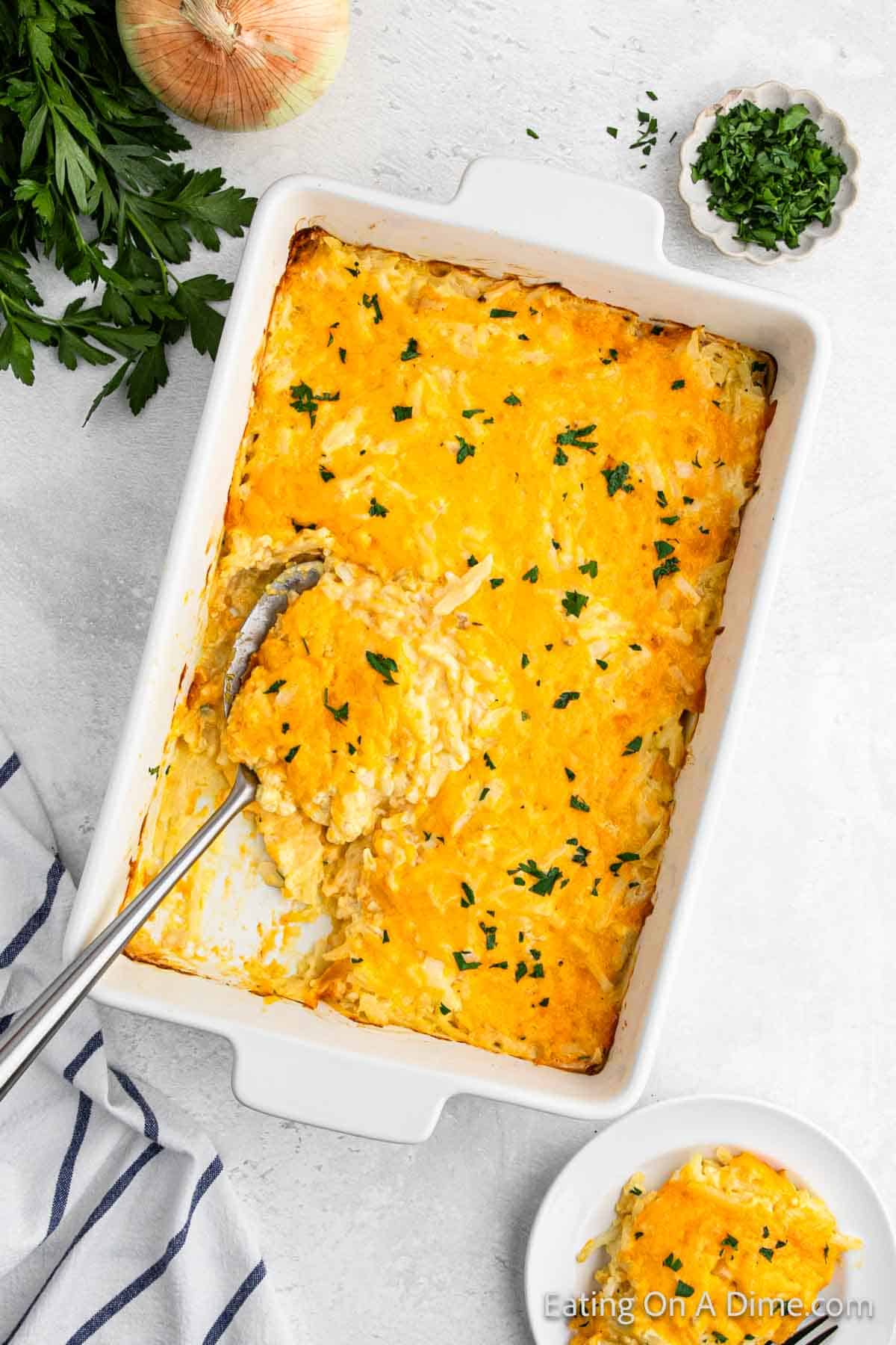 Cheesy potato casserole in a baking dish with a serving on a silver spoon