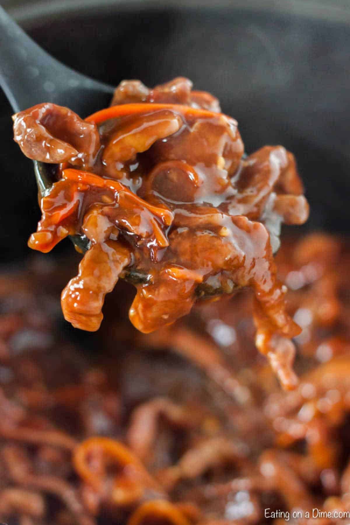 Close-up of a spoon lifting tender Mongolian beef strips from a slow cooker. The beef glistens with a rich, glossy sauce, hinting at a flavorful and savory dish.