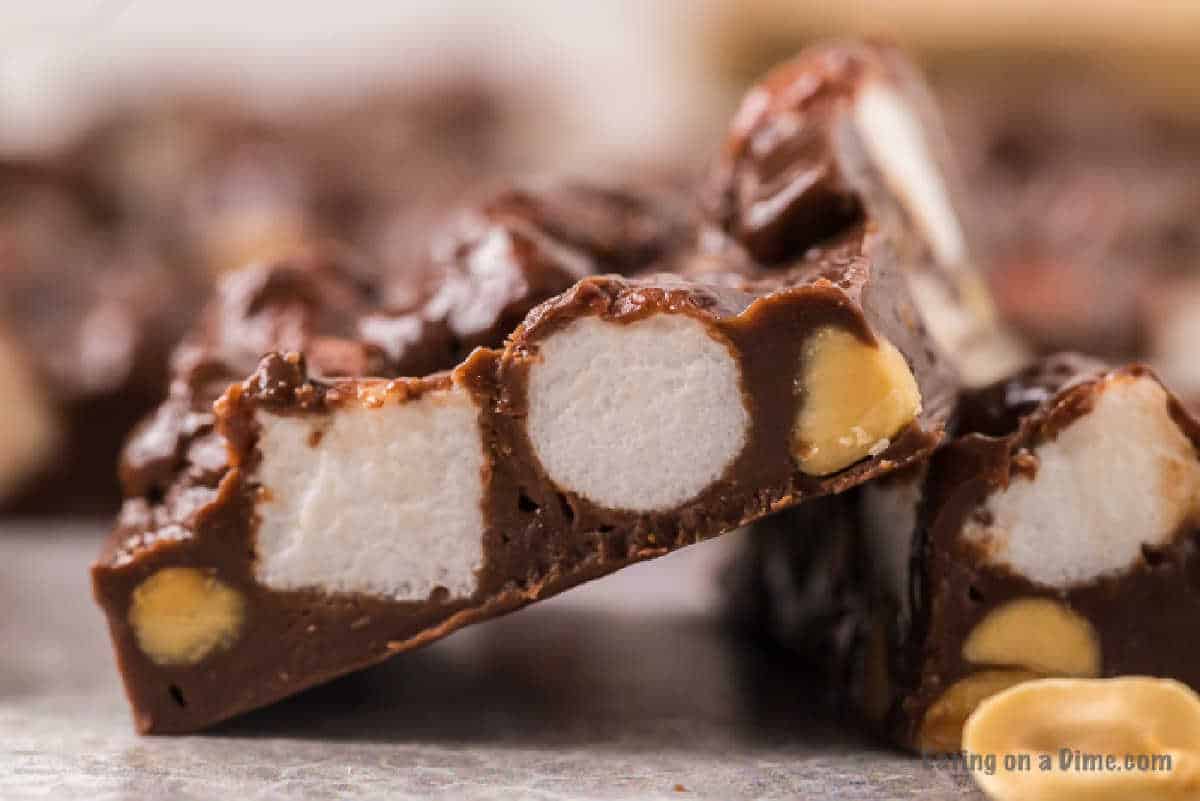 Close-up of a slice of chocolate fudge filled with marshmallows and nuts. The rich chocolate is visibly interspersed with large, white marshmallow chunks and whole nuts, reminiscent of an easy rocky road fudge recipe, creating a textured and indulgent treat.