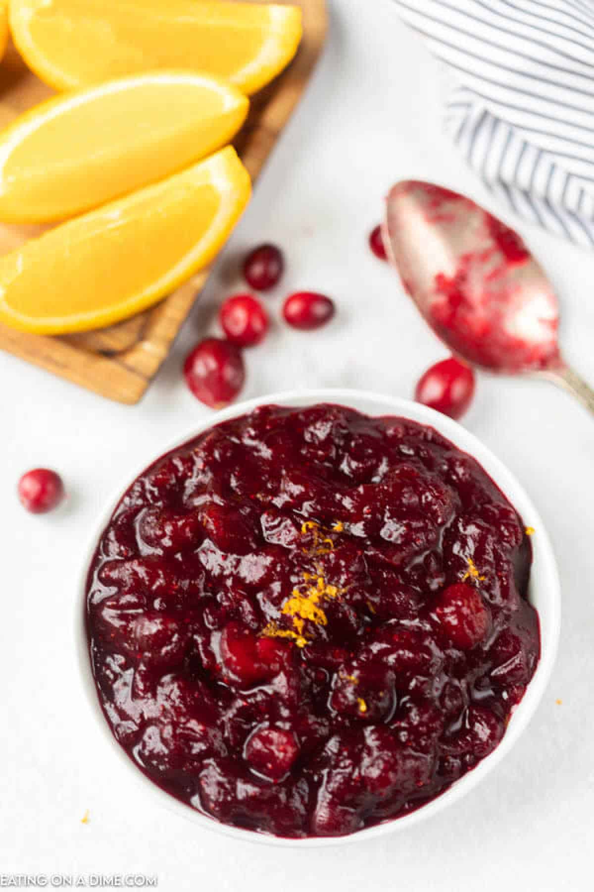 Cranberry sauce in a bowl with slice lemons in the background with cranberries on the side