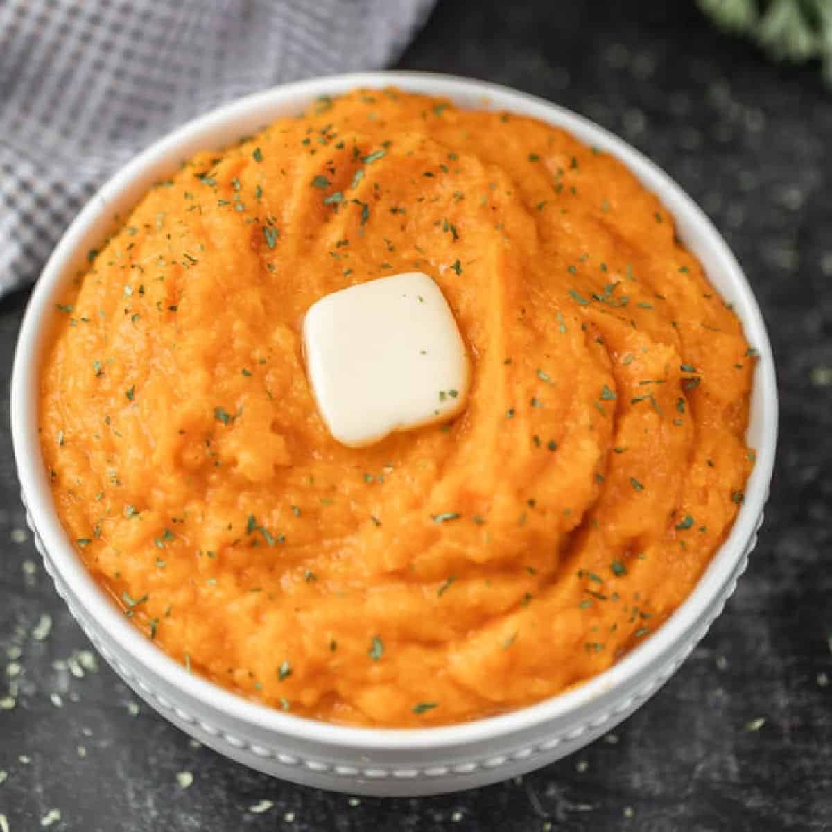 Bowl of mashed sweet potatoes topped with butter. 