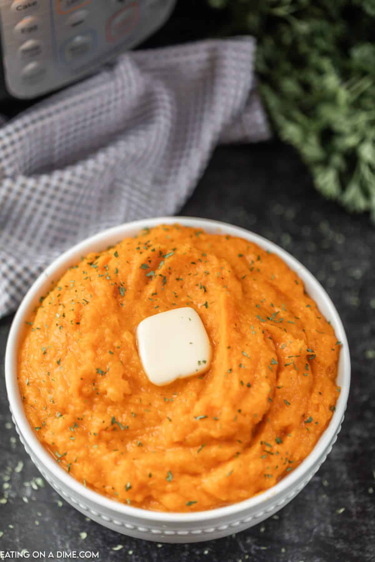 Bowl of mashed sweet potatoes topped with butter. 