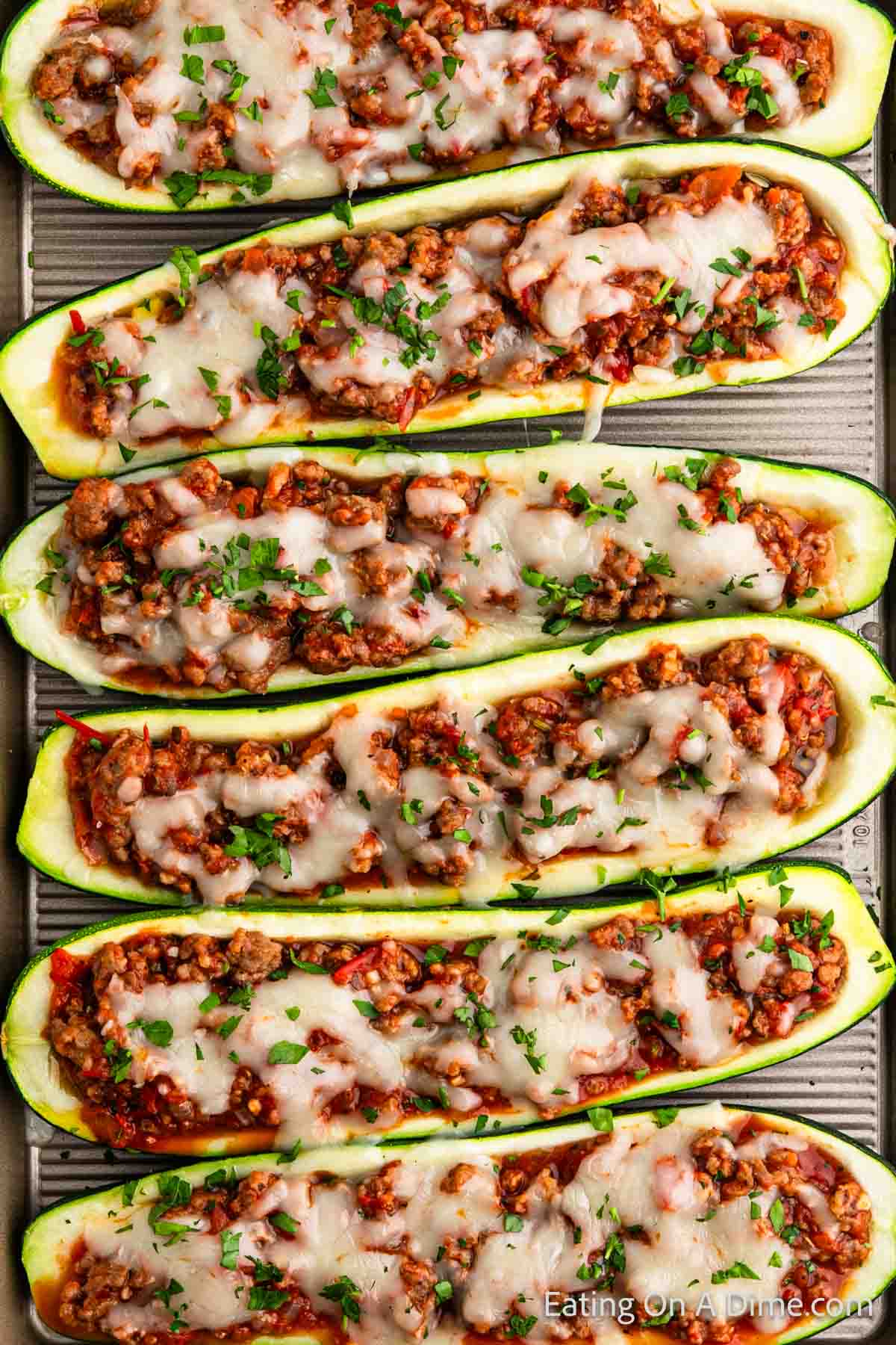 A baking tray filled with zucchini boats stuffed with a hearty mixture of ground meat, diced vegetables, and topped with melted cheese and freshly chopped herbs—the perfect stuffed zucchini boats recipe.