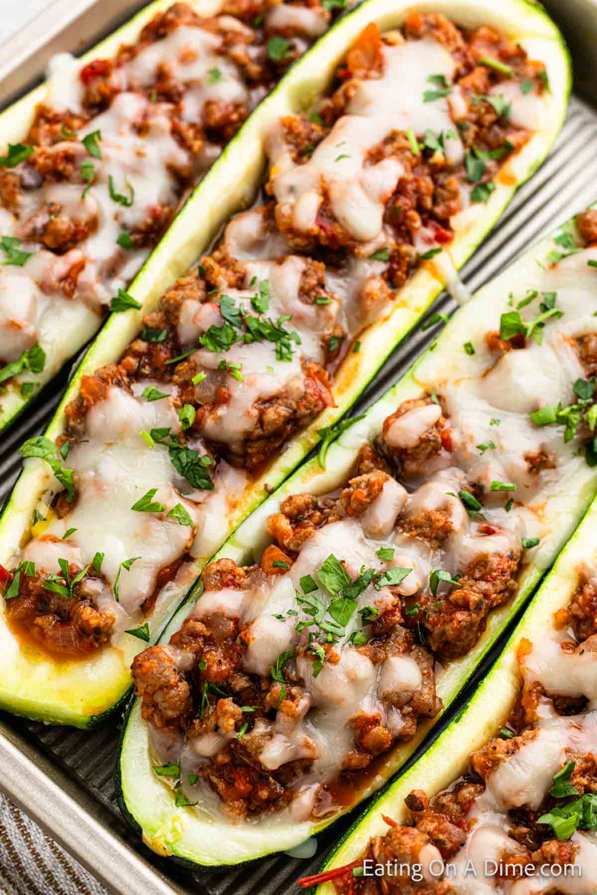 A close-up of zucchini boats stuffed with a savory ground meat and tomato mixture, topped with melted cheese and sprinkled with fresh chopped parsley. The stuffed zucchini boats recipe is beautifully arranged in a baking dish.