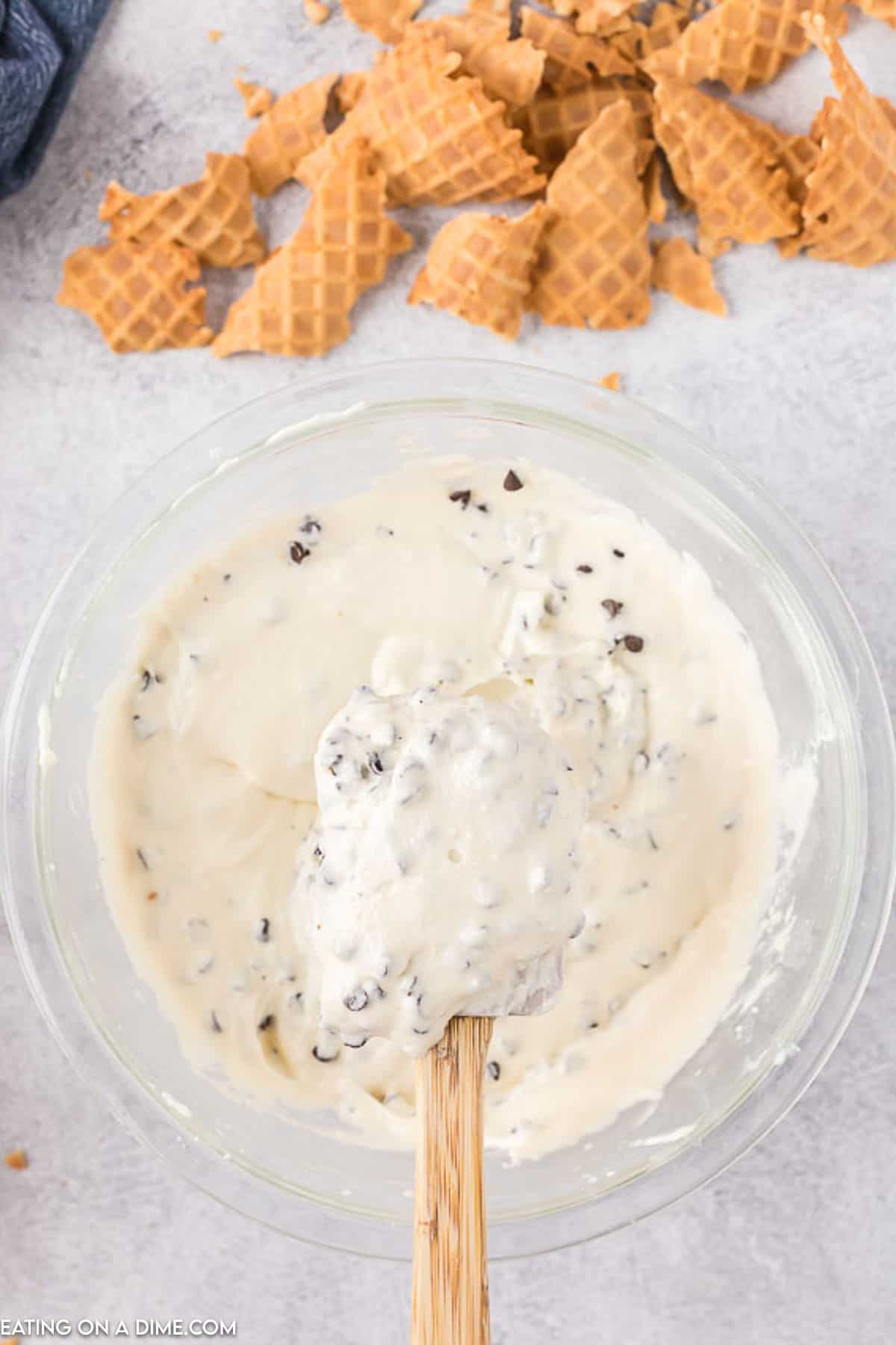 Chocolate chips mixed into the dip batter with a serving on a wooden spoon and cone chips on the side