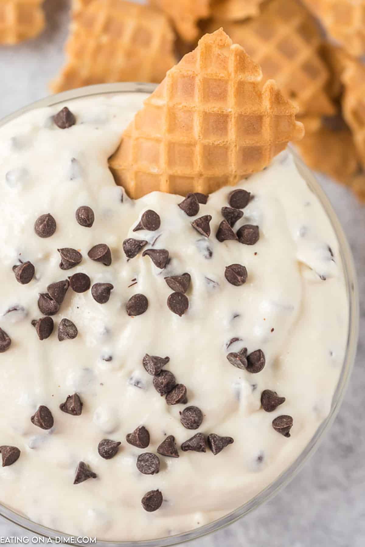 Cannoli Dip in a bowl topped with chocolate chips with a piece of cone in the dip