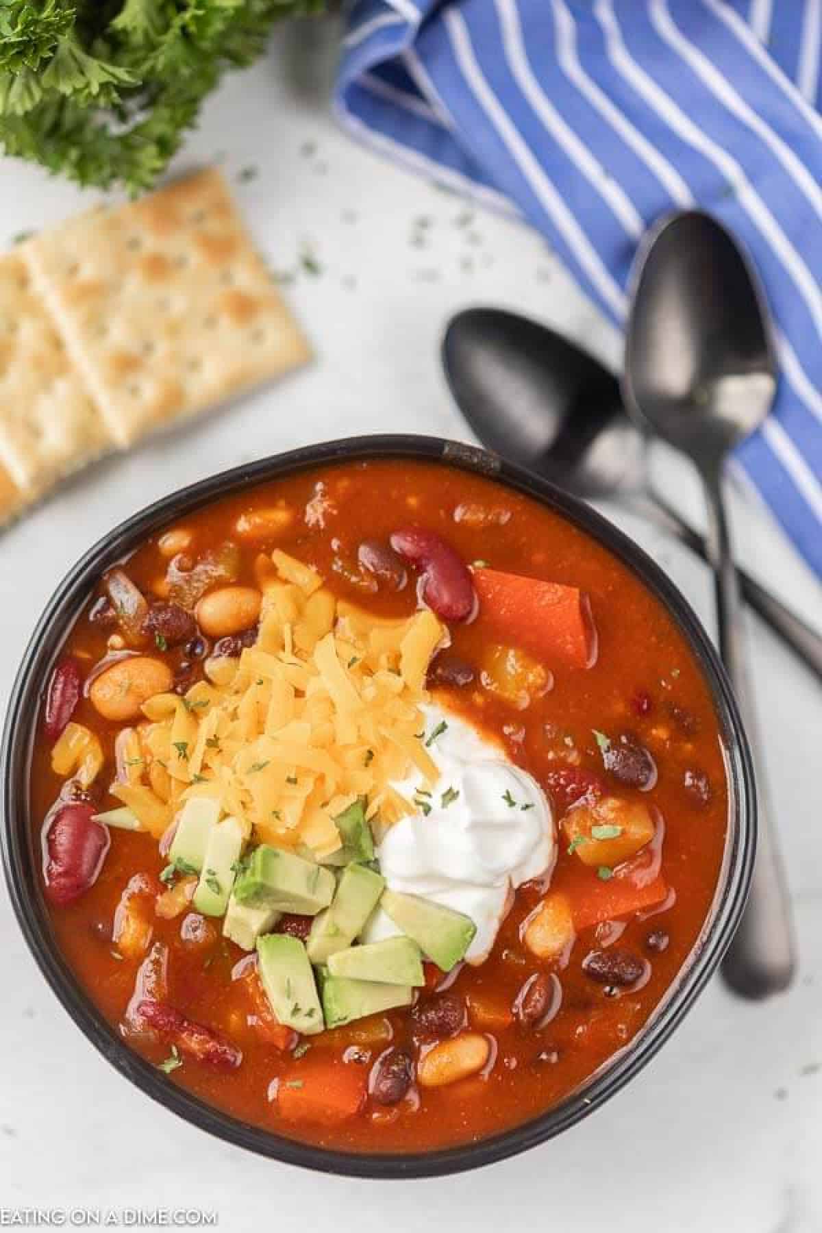 Close up image of vegetarian chili in a black bowl with crackers and two spoons. 