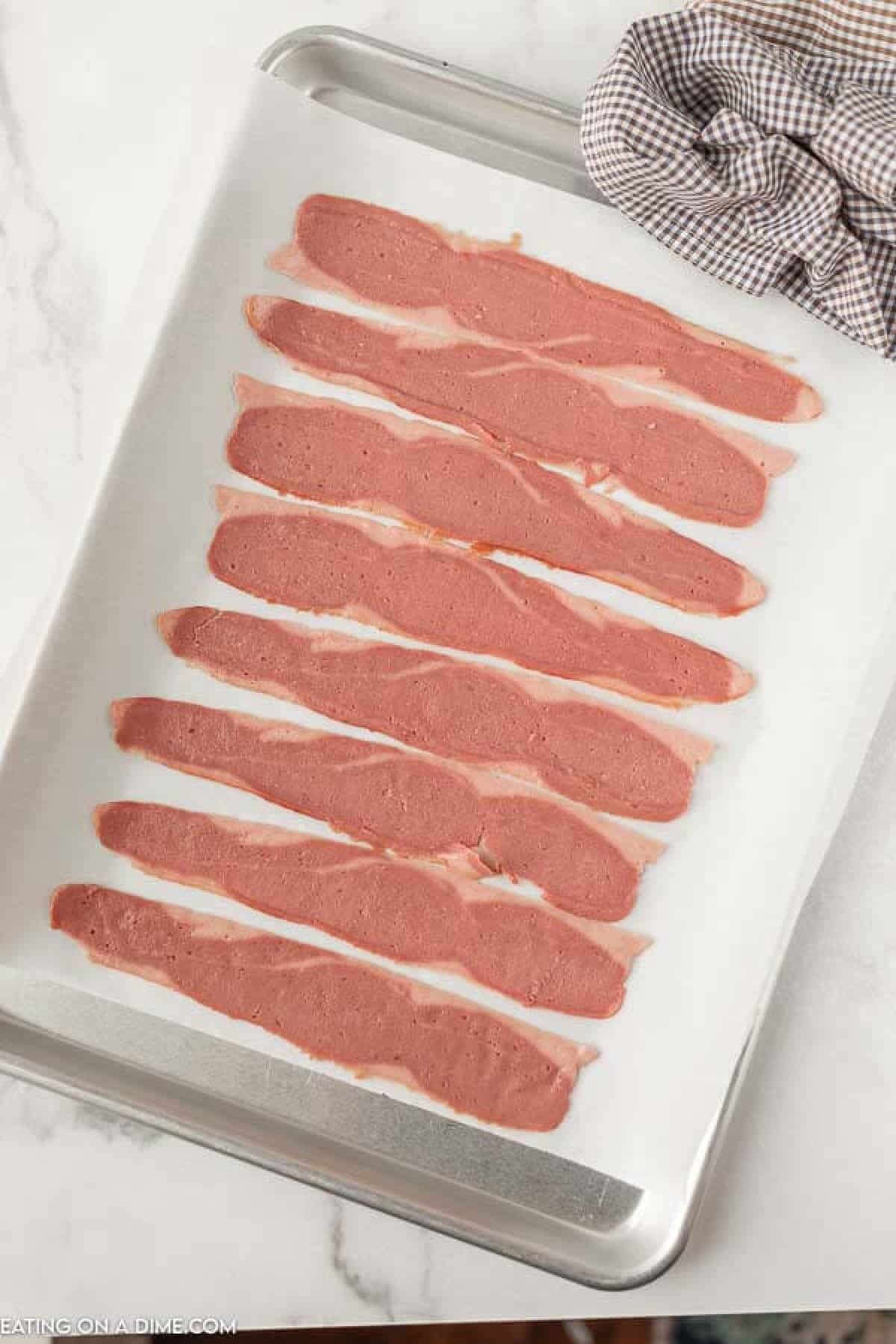 Close up image of uncooked turkey bacon on a baking sheet. 