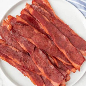 A plate with neatly arranged crispy turkey bacon strips on a white round dish, set on a light background, showcasing how to bake turkey bacon to perfection.