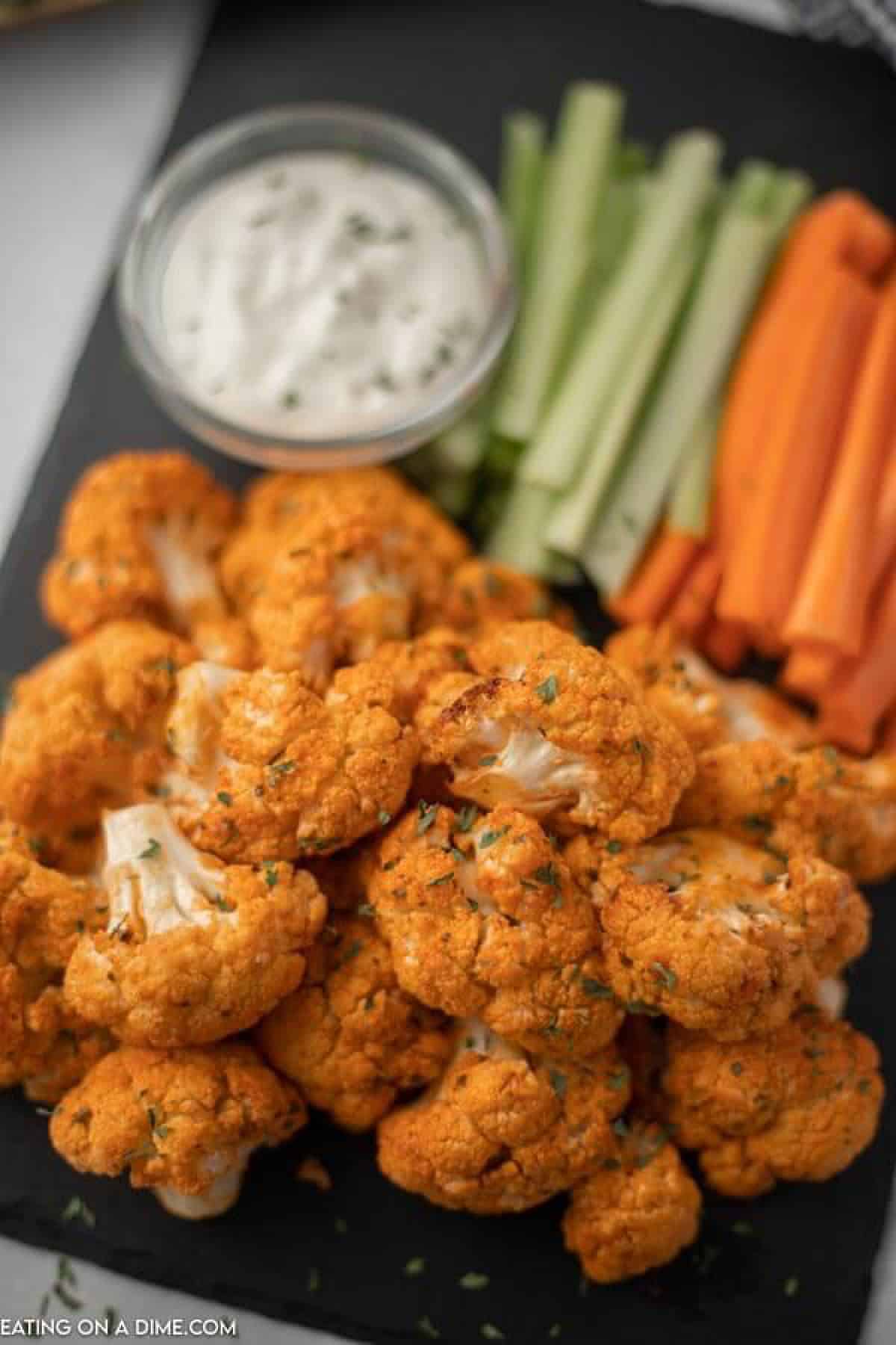 Close up image of buffalo cauliflower on a serving tray with ranch dip and carrots and celery. 