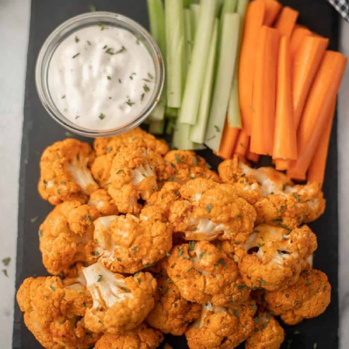 Close up image of buffalo cauliflower on a serving tray with ranch dip and carrots and celery. 