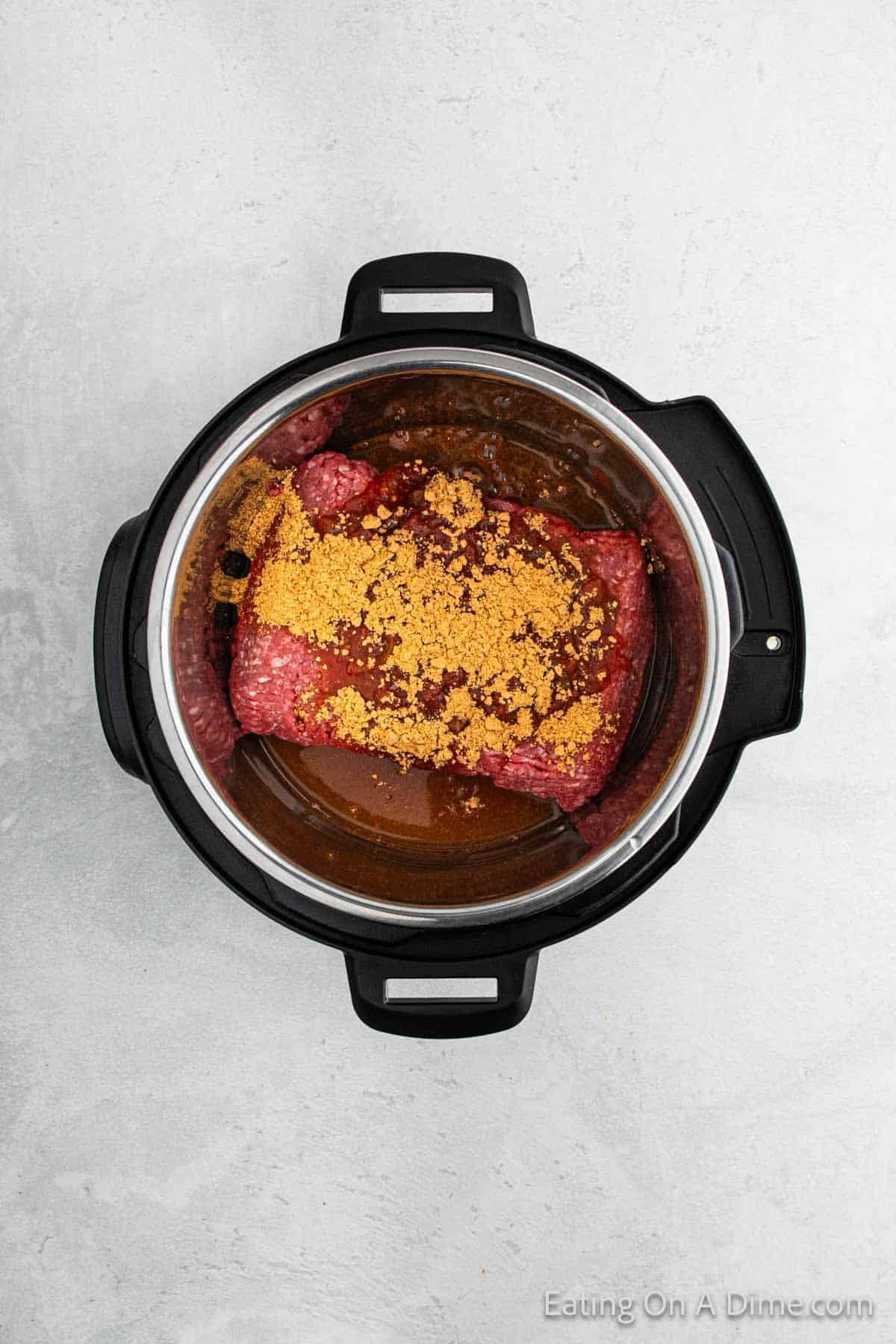 An overhead view of Instant Pot Taco Meat featuring raw ground beef topped with a sprinkle of spices and seasonings, set on a textured gray surface.