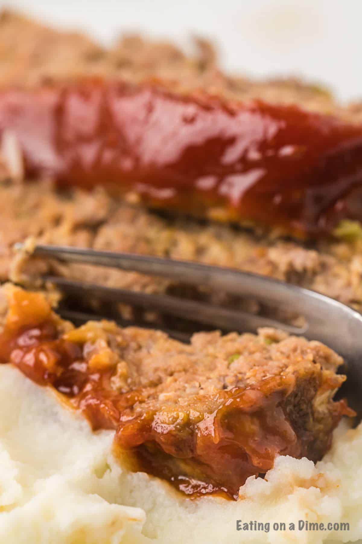 Close up image of meatloaf with a side of mashed potatoes with a fork. 