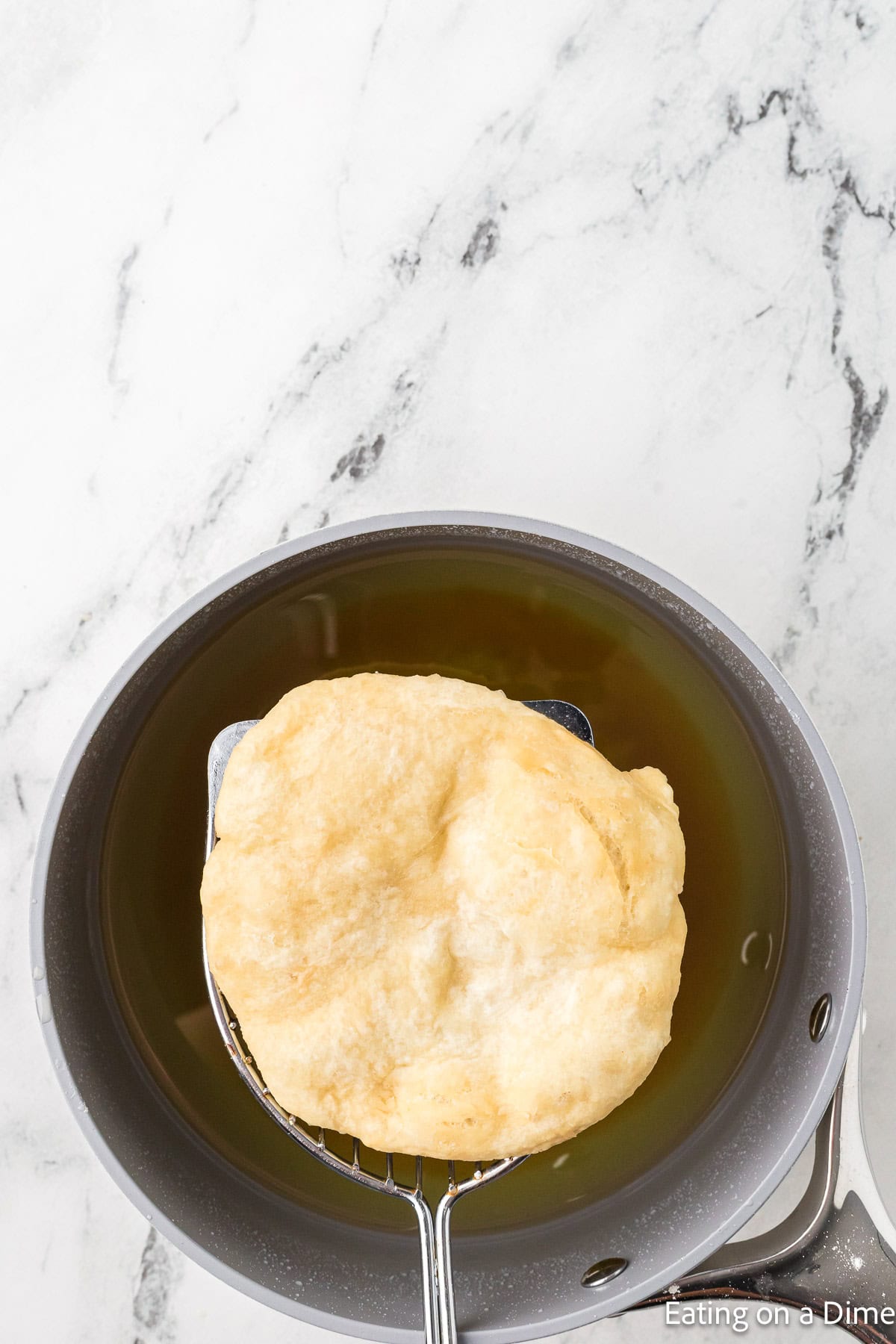 Fried bread on a silver spatula over a skillet with oil