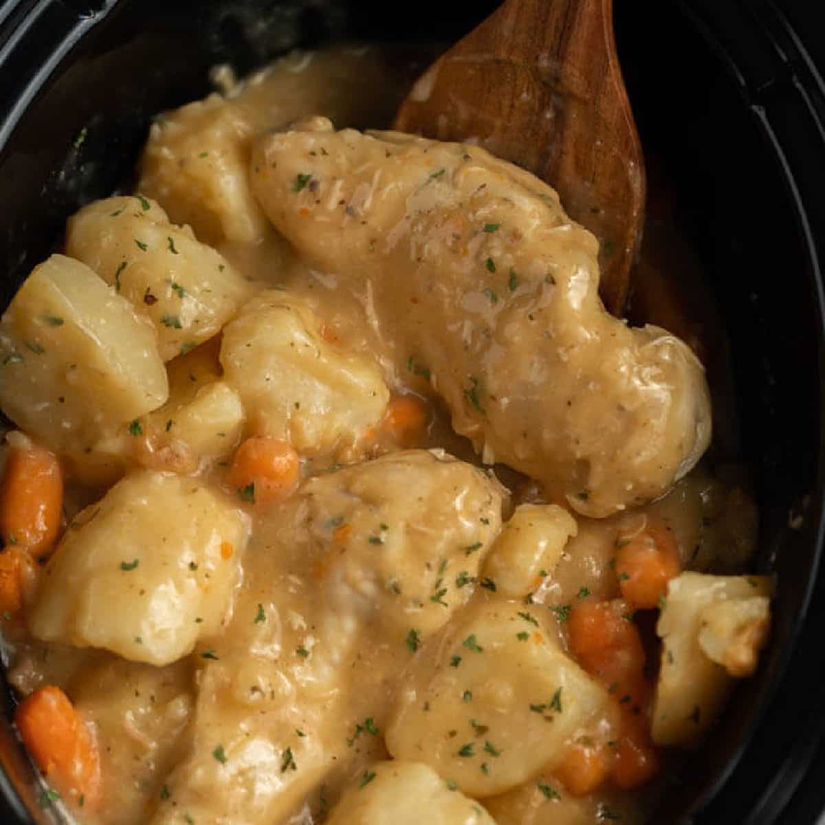 Ranch Chicken in the crock pot with a wooden spoon. 