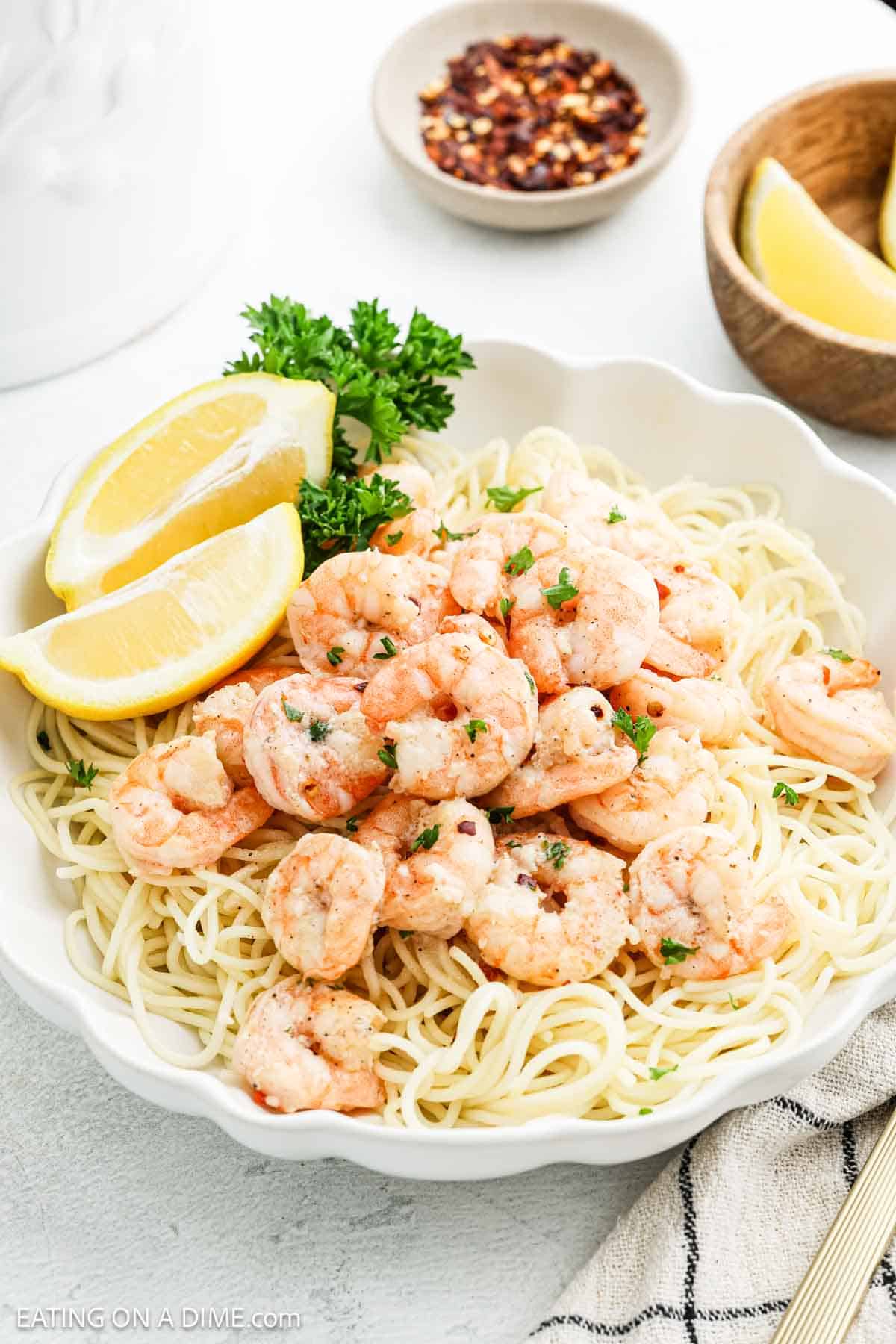 Shrimp Scampi topped spaghetti noodles in a bowl topped with lemon wedges and fresh parsley