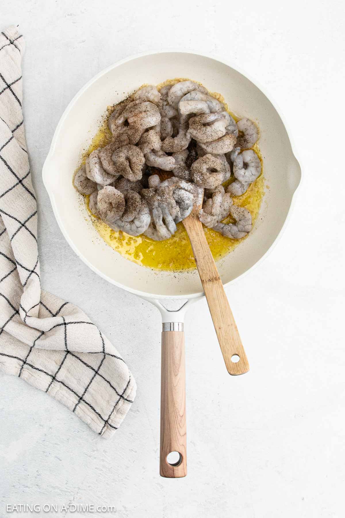 Uncooked shrimp in the skillet with melted butter topped with seasoning