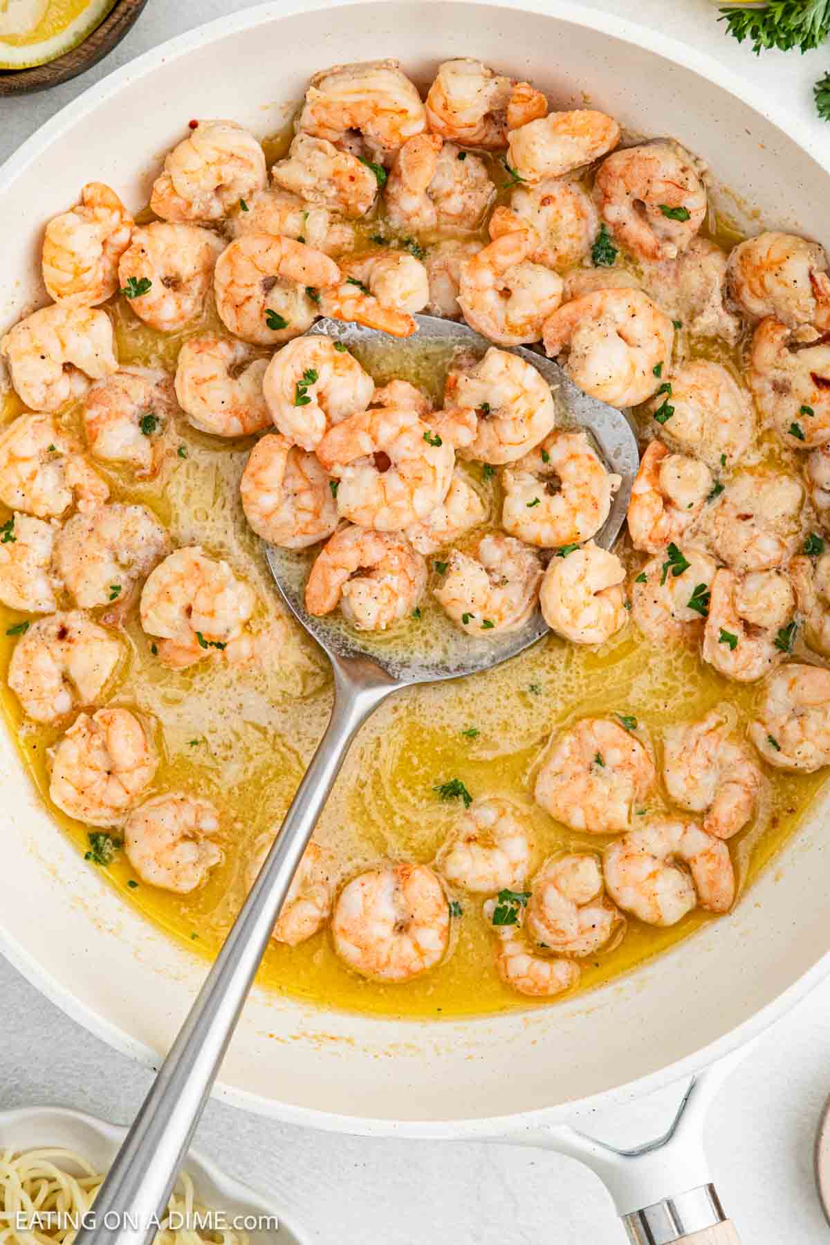 Cooked Shrimp in a skillet in a melted butter sauce with a silver spoon