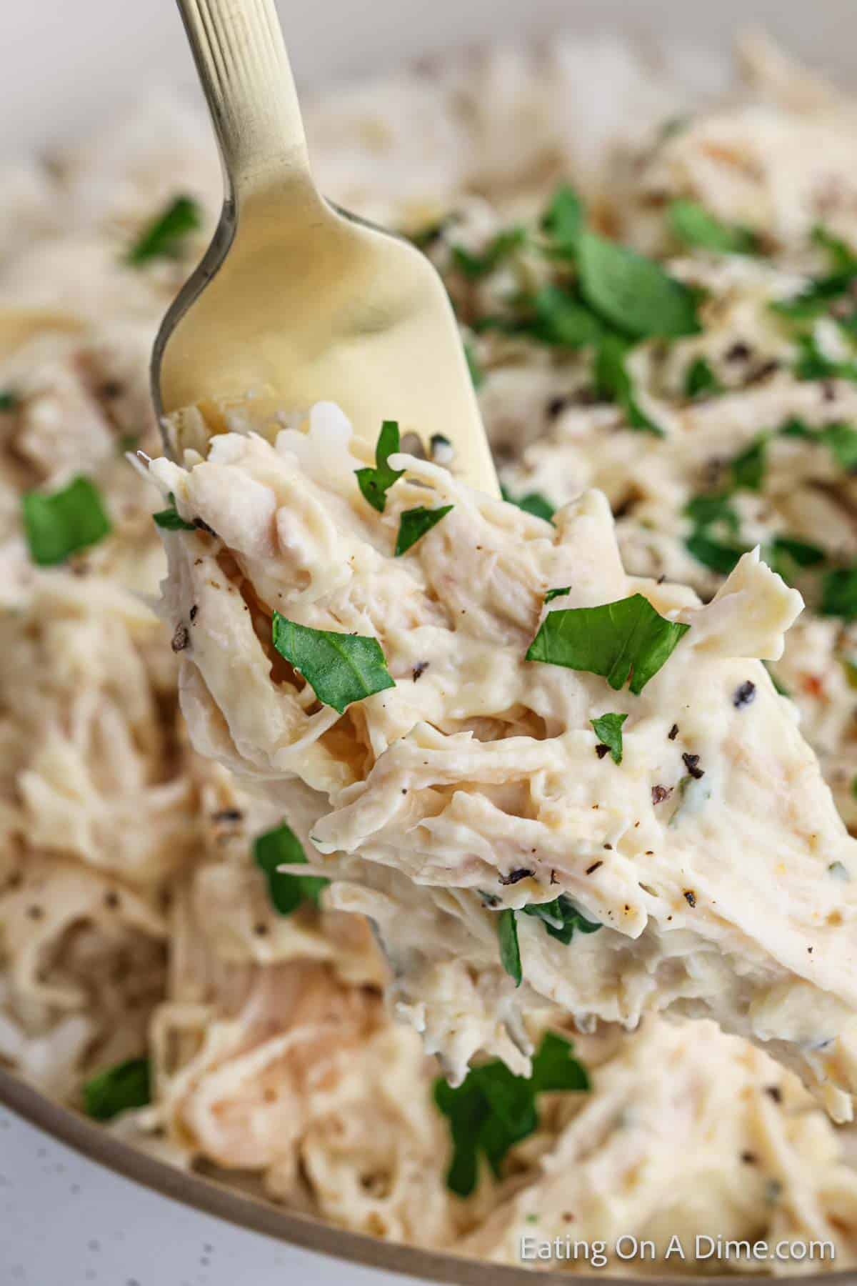 A fork holds a serving of creamy shredded chicken mixed with herbs and spices from a Slow Cooker Italian Chicken Recipe. The dish is garnished with fresh parsley, adding a pop of green against the creamy texture of the chicken.