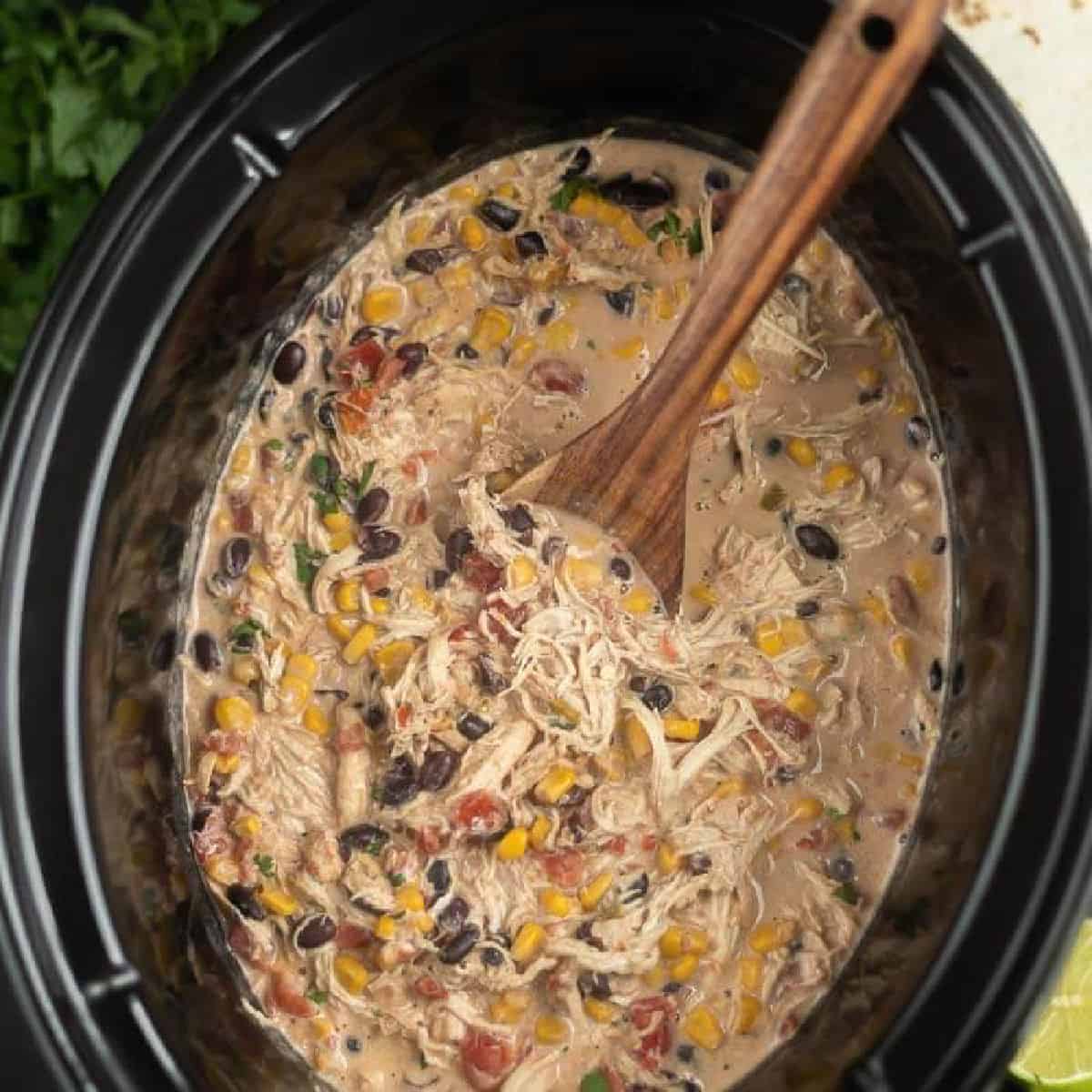 Close up image of fiesta chicken in the crock pot with a wooden spoon.