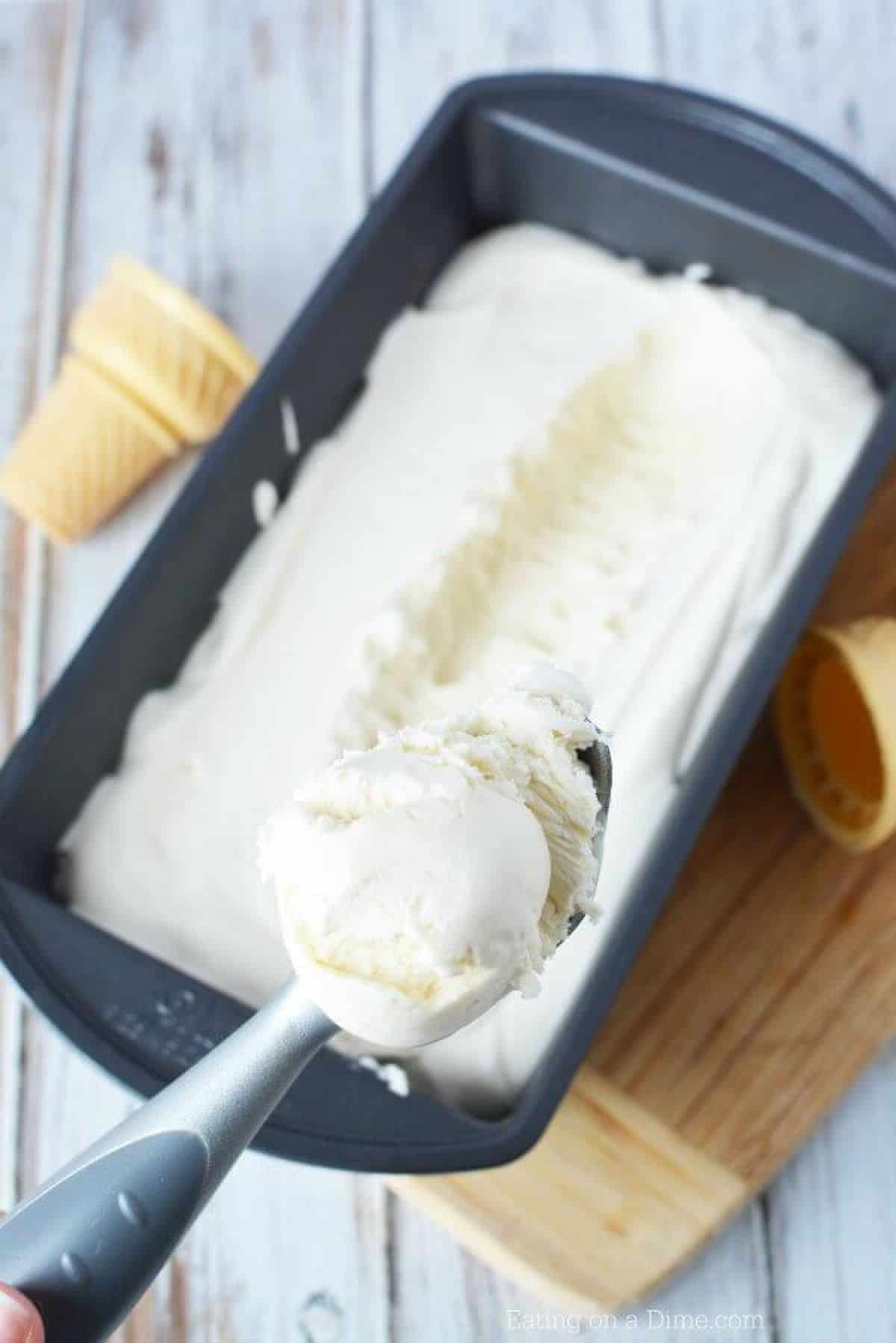 Homemade vanilla ice cream in a loaf pan with an ice cream scoop scooping out a portion of the ice cream.  