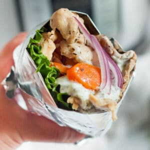 A close-up of a gyro wrapped in foil, brimming with Instant Pot chicken, lettuce, sliced carrots, red onion, and a creamy sauce.