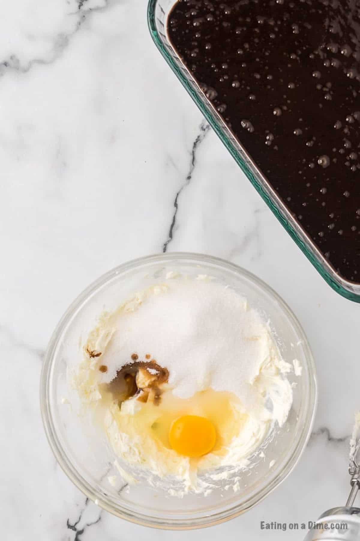 Bowl with egg, vanilla and sugar with the cream cheese and a baking dish with the brownie batter