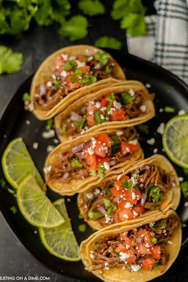 Close up image of street tacos on a plate with a side of limes. 