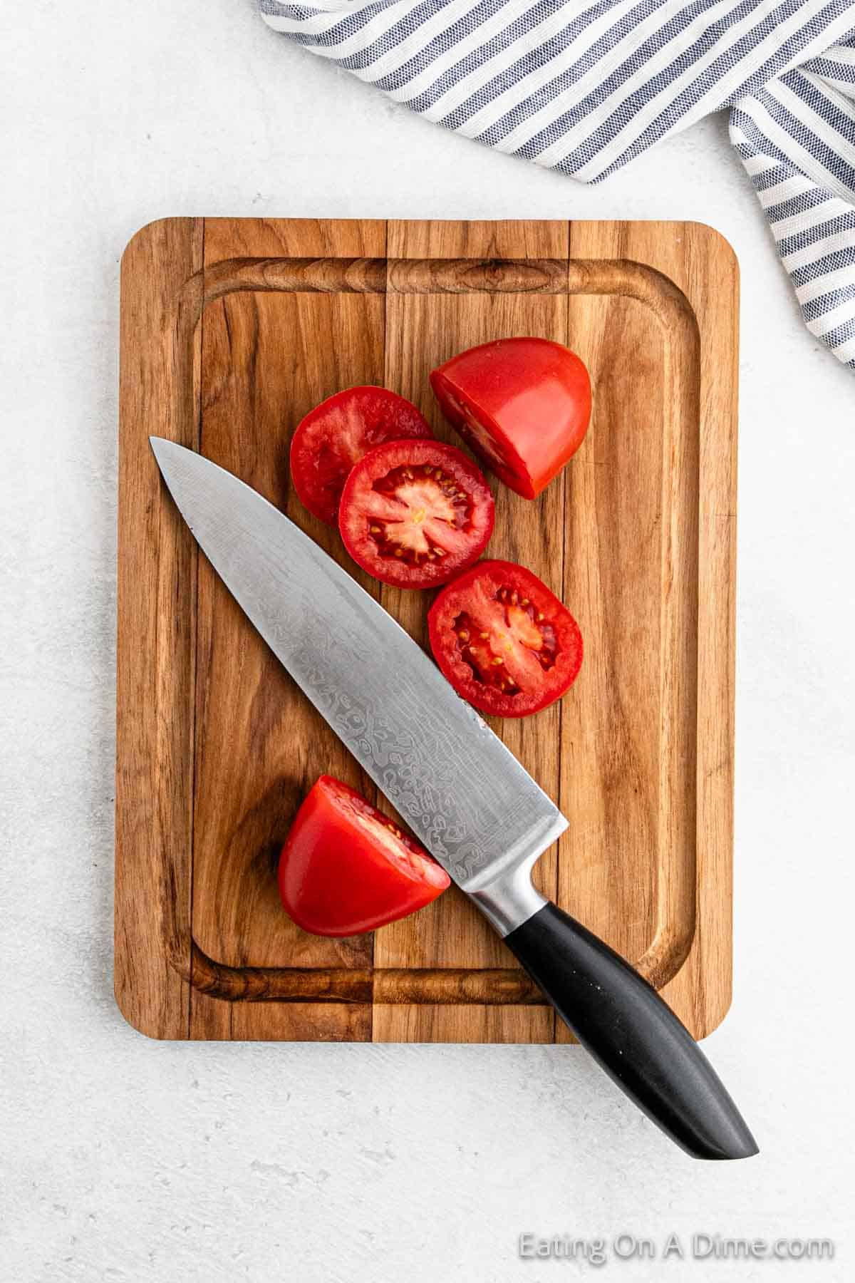 A wooden cutting board with a chef's knife and sliced red tomatoes, perfect for an easy Pico de Gallo, is on display. A striped cloth is partially visible in the top right corner.