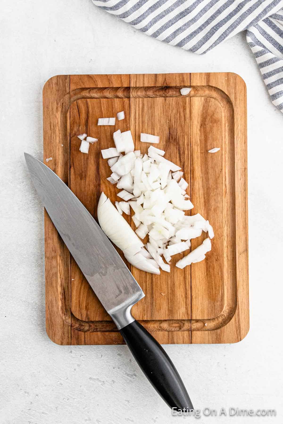 Chopped onions and a kitchen knife rest on a wooden cutting board, ready to transform into an easy Pico De Gallo. A striped cloth lies nearby, adding a touch of charm to the culinary scene.