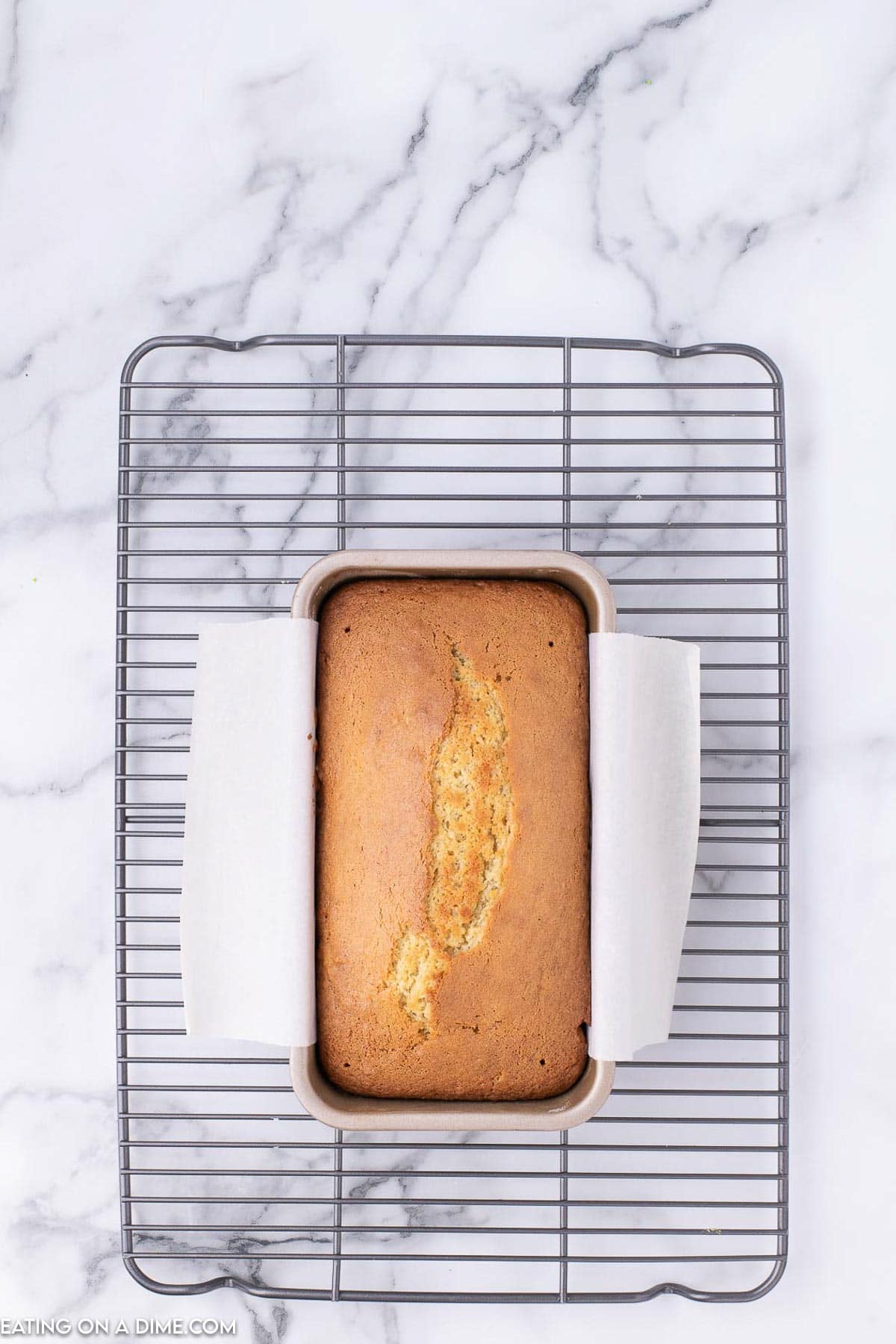 Baked lemon loaf in a loaf pan lined with parchment paper on a wire rack
