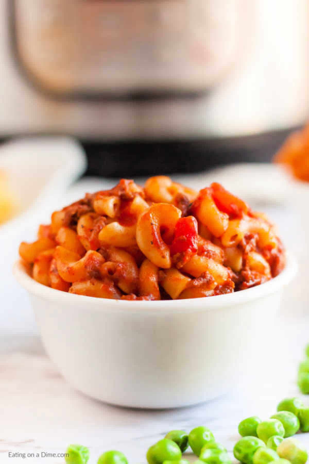 Goulash in a white bowl with a side of green peas. 