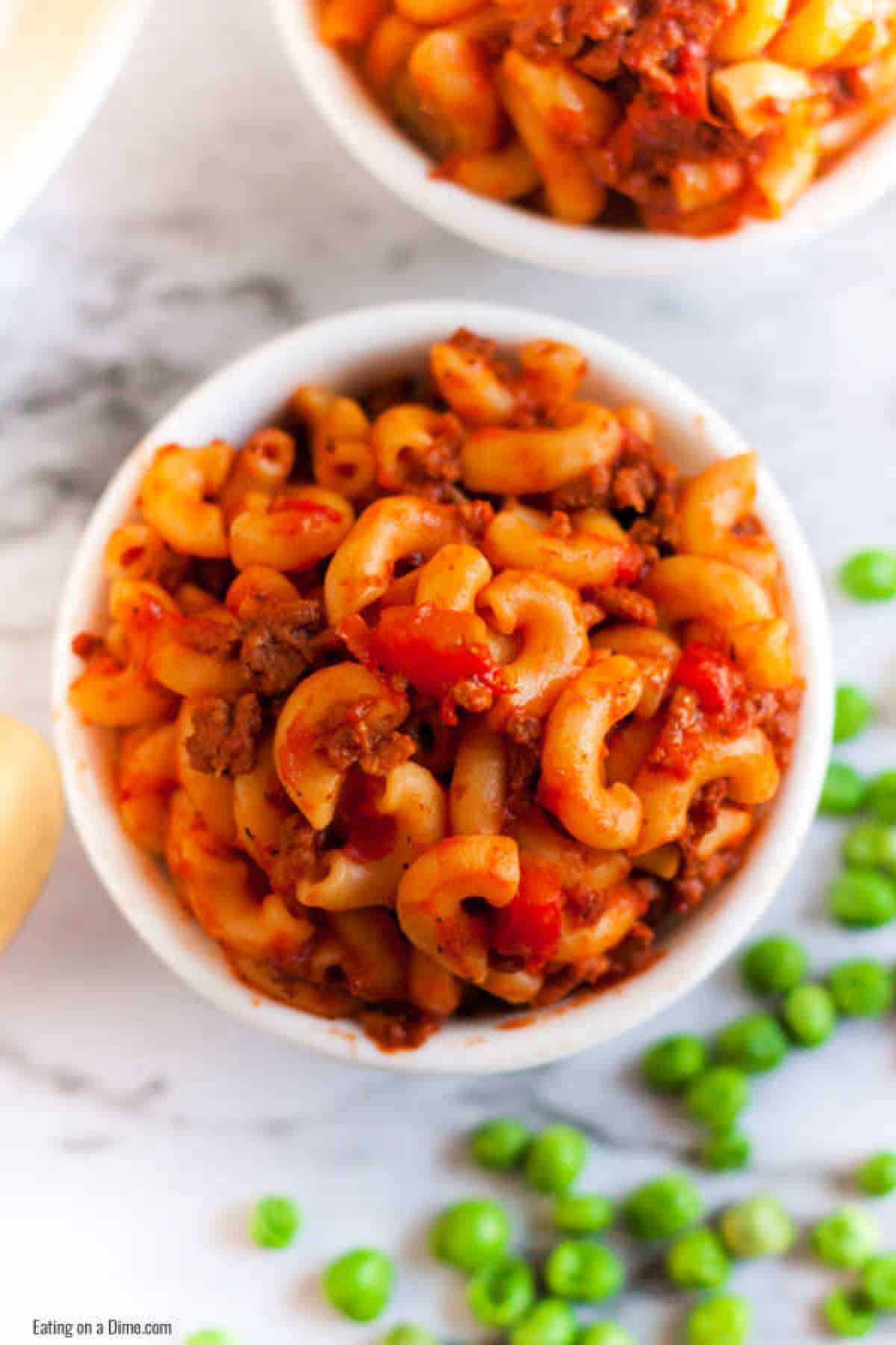 Goulash in a white bowl with a side of green peas. 