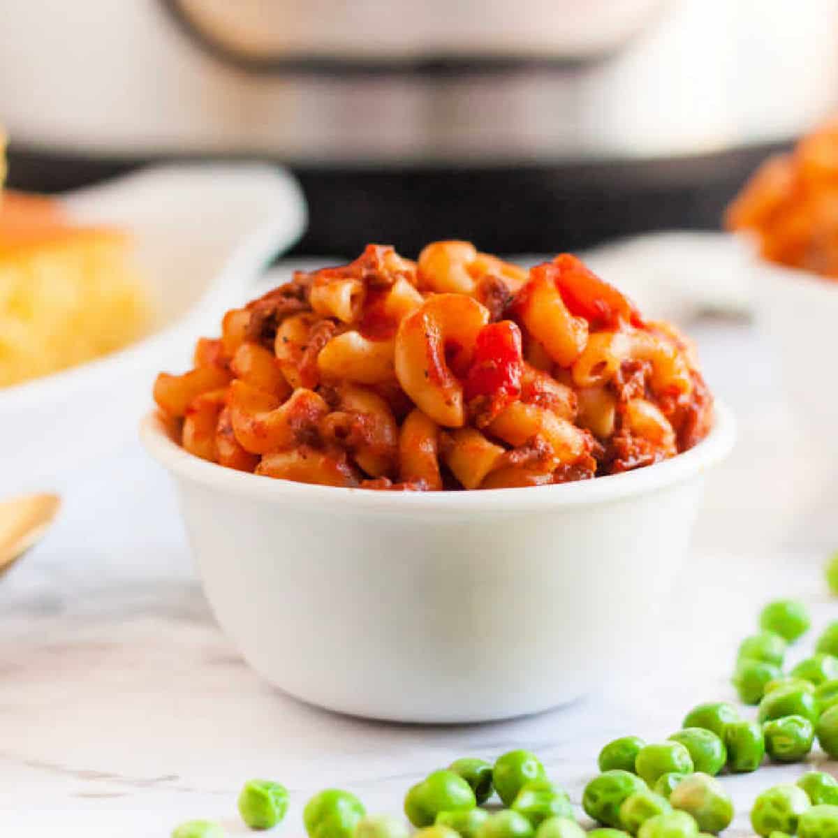 Goulash in a white bowl with a side of green peas. 