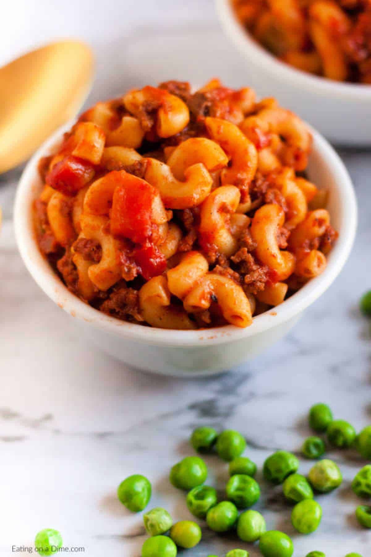 Goulash in a white bowl with a side of green peas. 